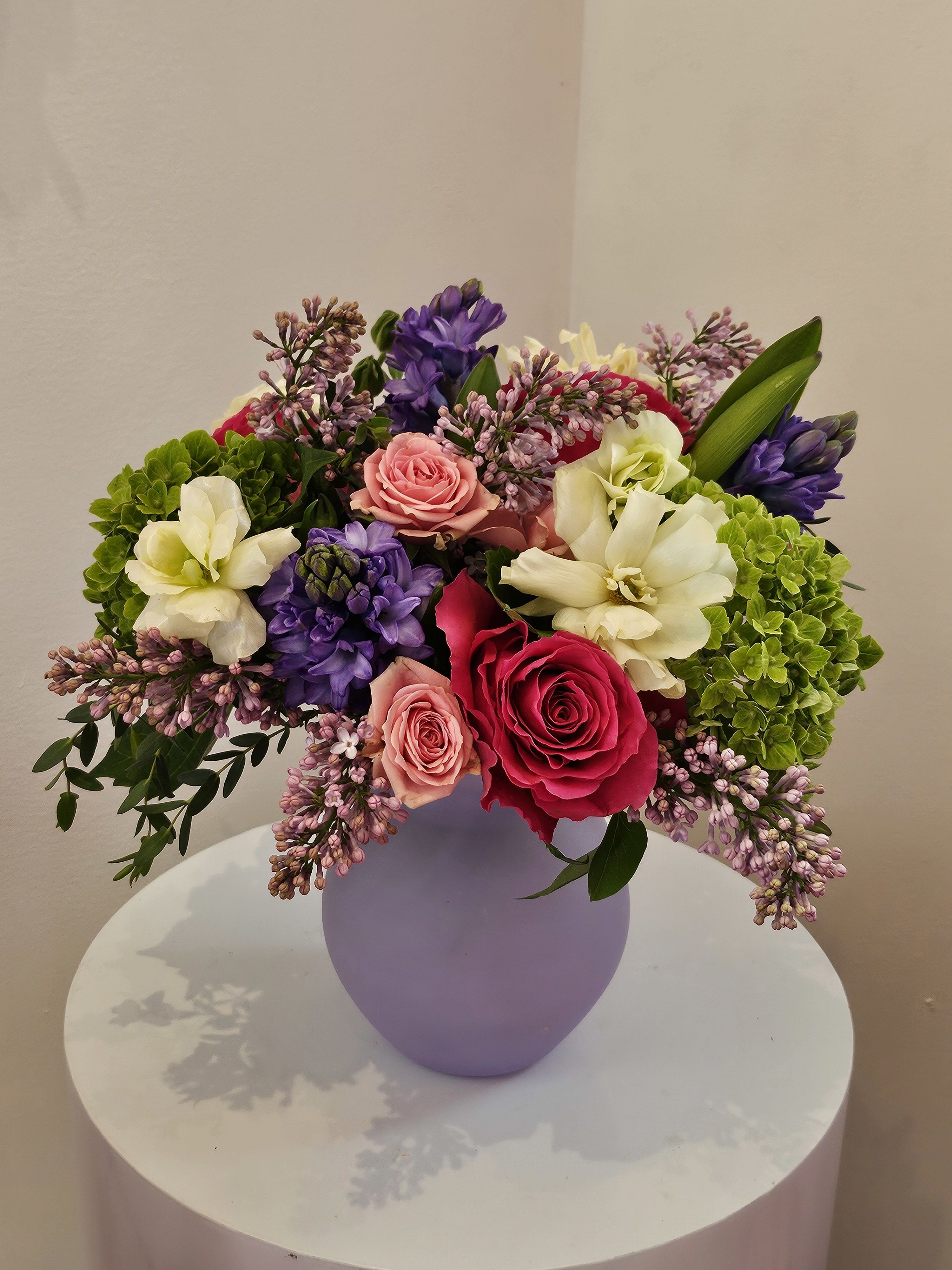 Mixed bouquet of roses, hyacinths, and hydrangeas in a lavender vase