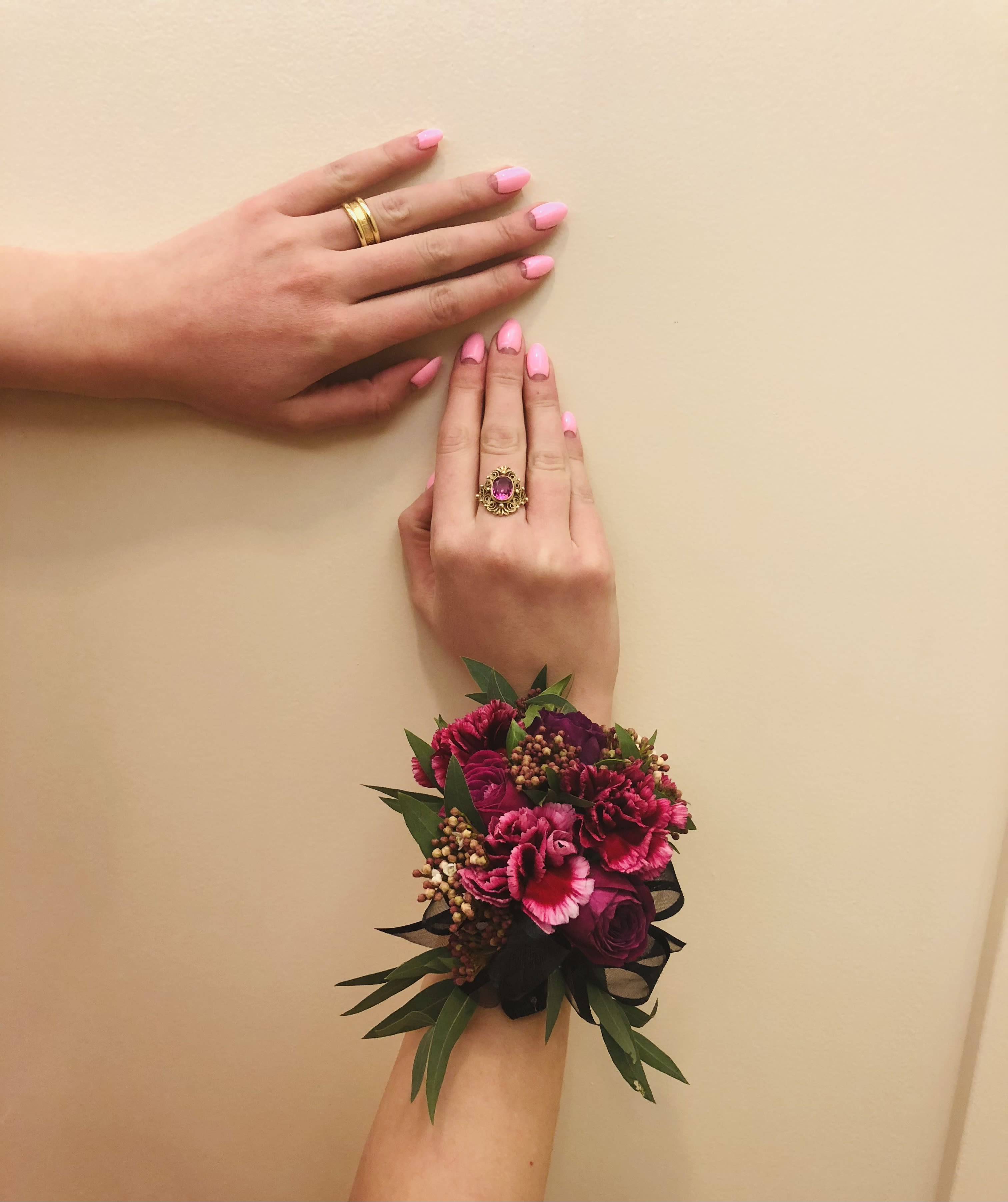 Pink floral wrist corsage with dark ribbon on a hand