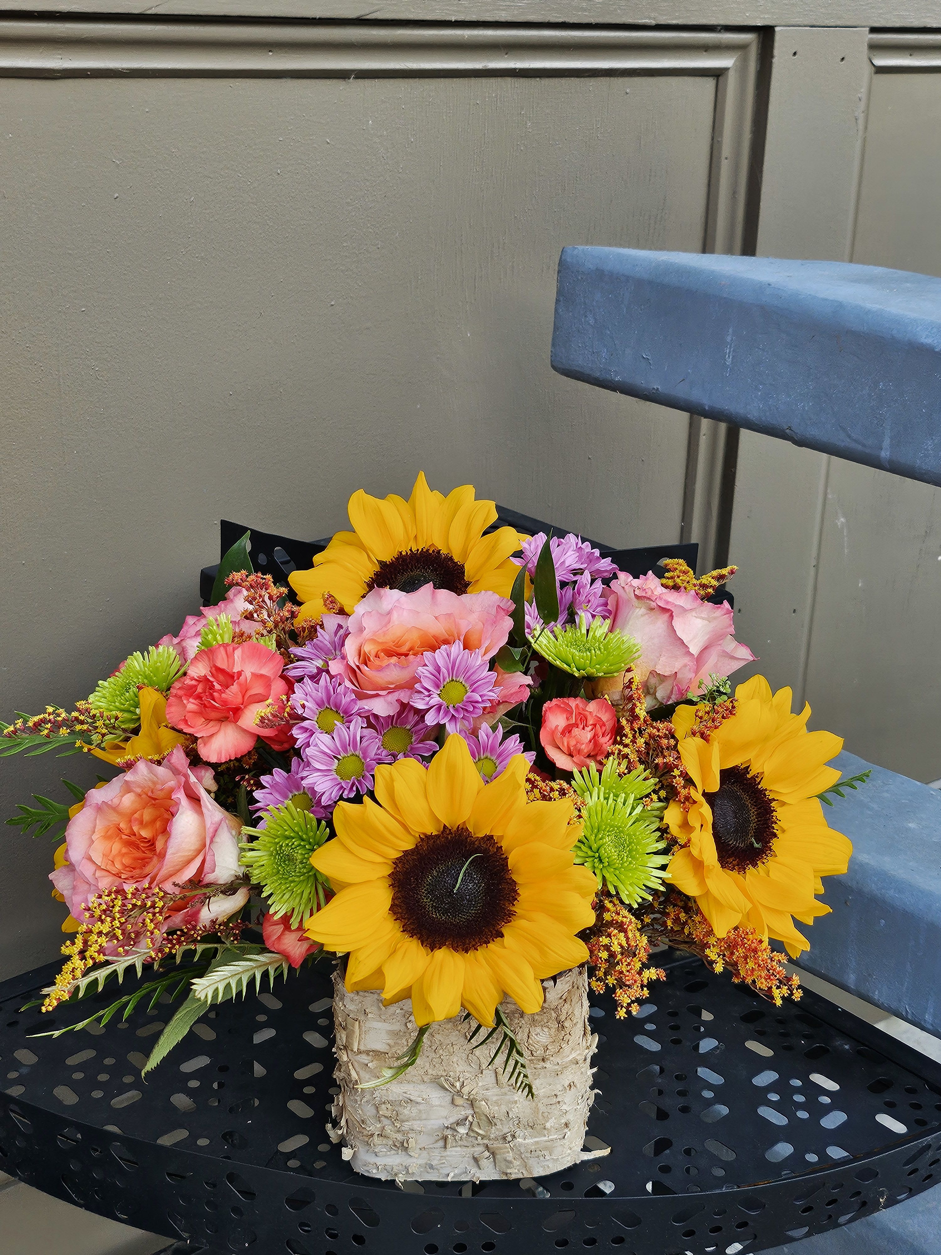 Bouquet of sunflowers, pink roses, and purple daisies in a birch container