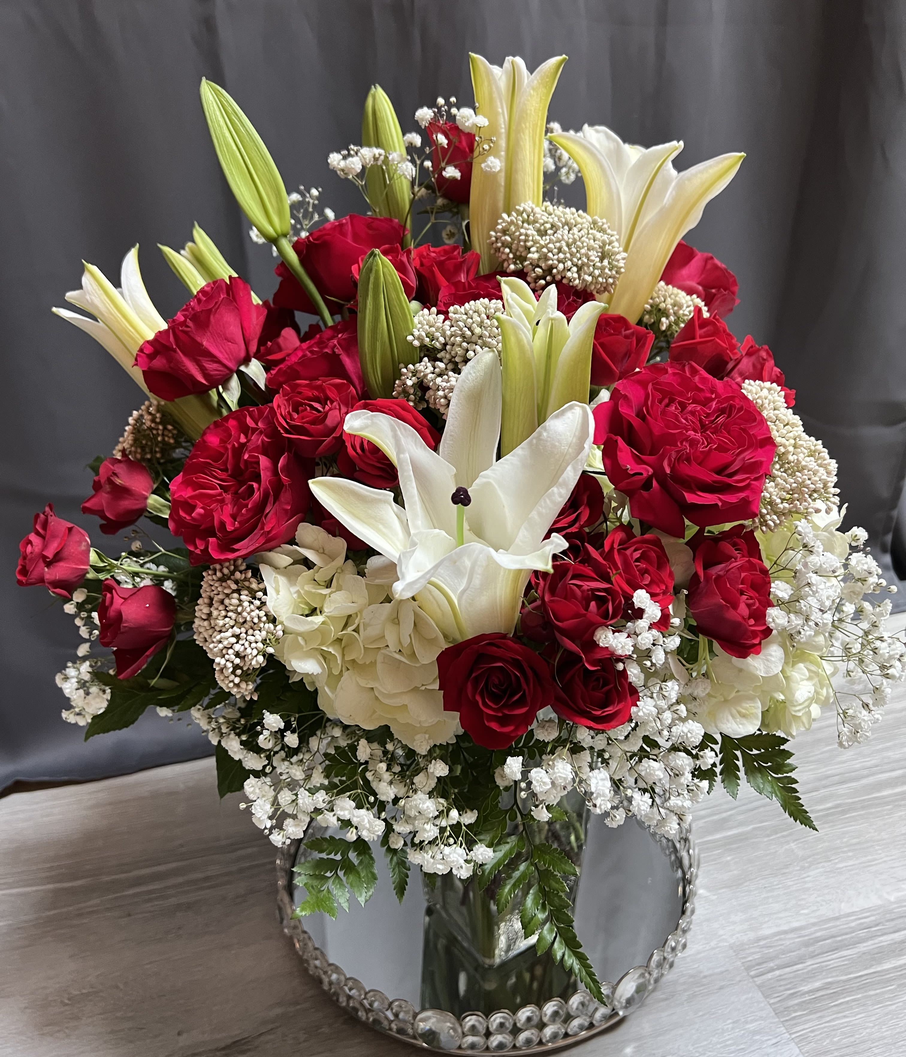 Red roses and white lilies in a mirrored vase with baby's breath