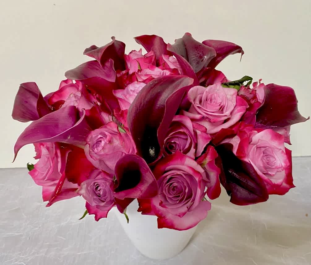 Pink roses and dark magenta calla lilies in a white vase