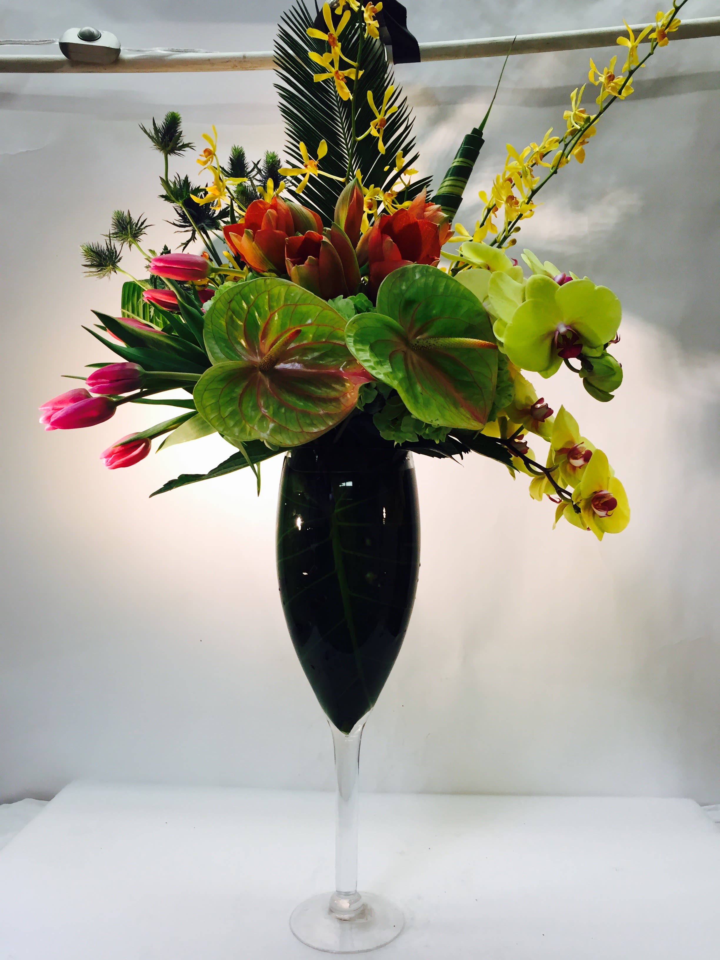 Tropical flower arrangement in a tall glass vase with orchids and tulips