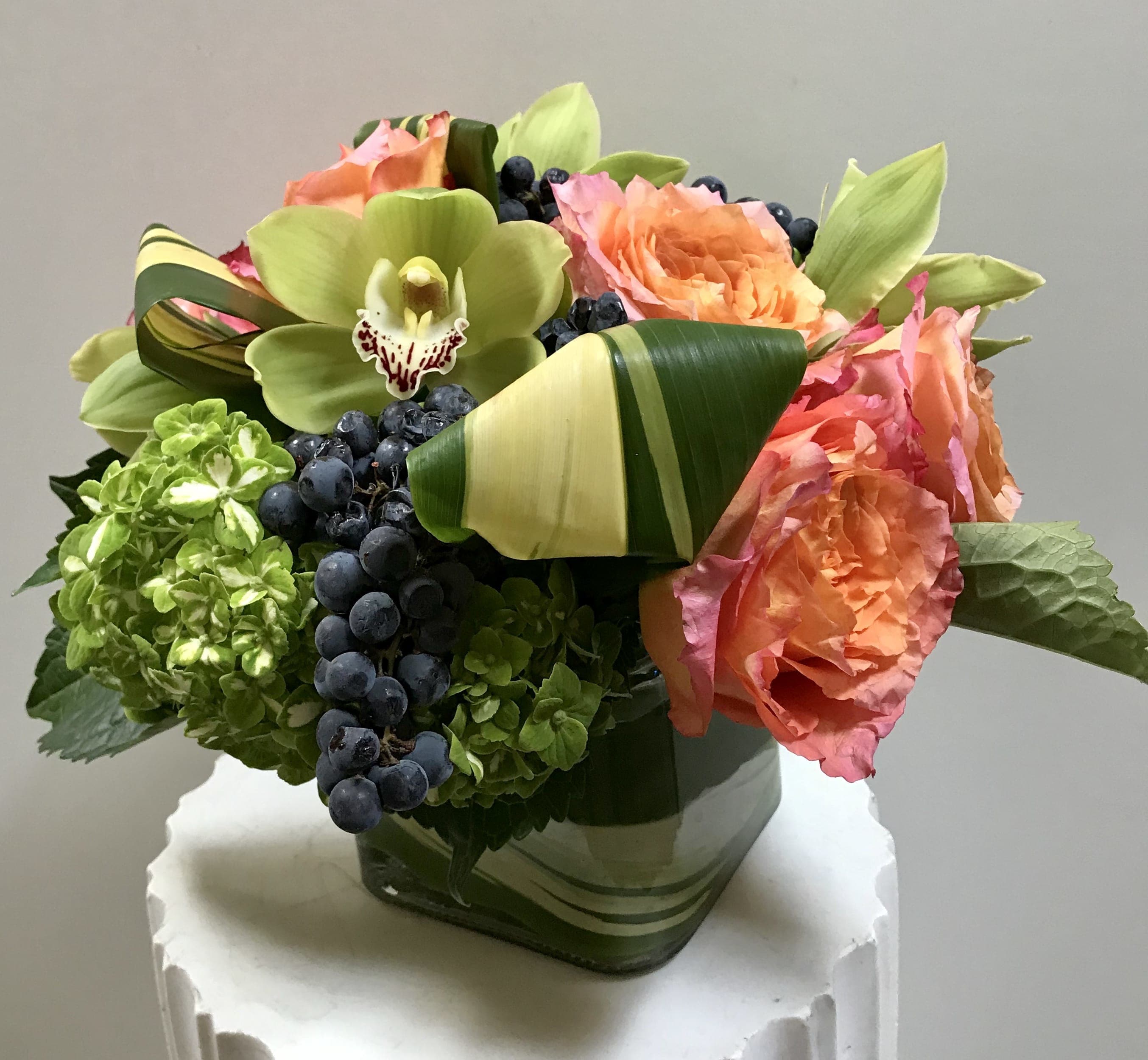 Bouquet of orange roses, green orchids, and hydrangeas in a square vase