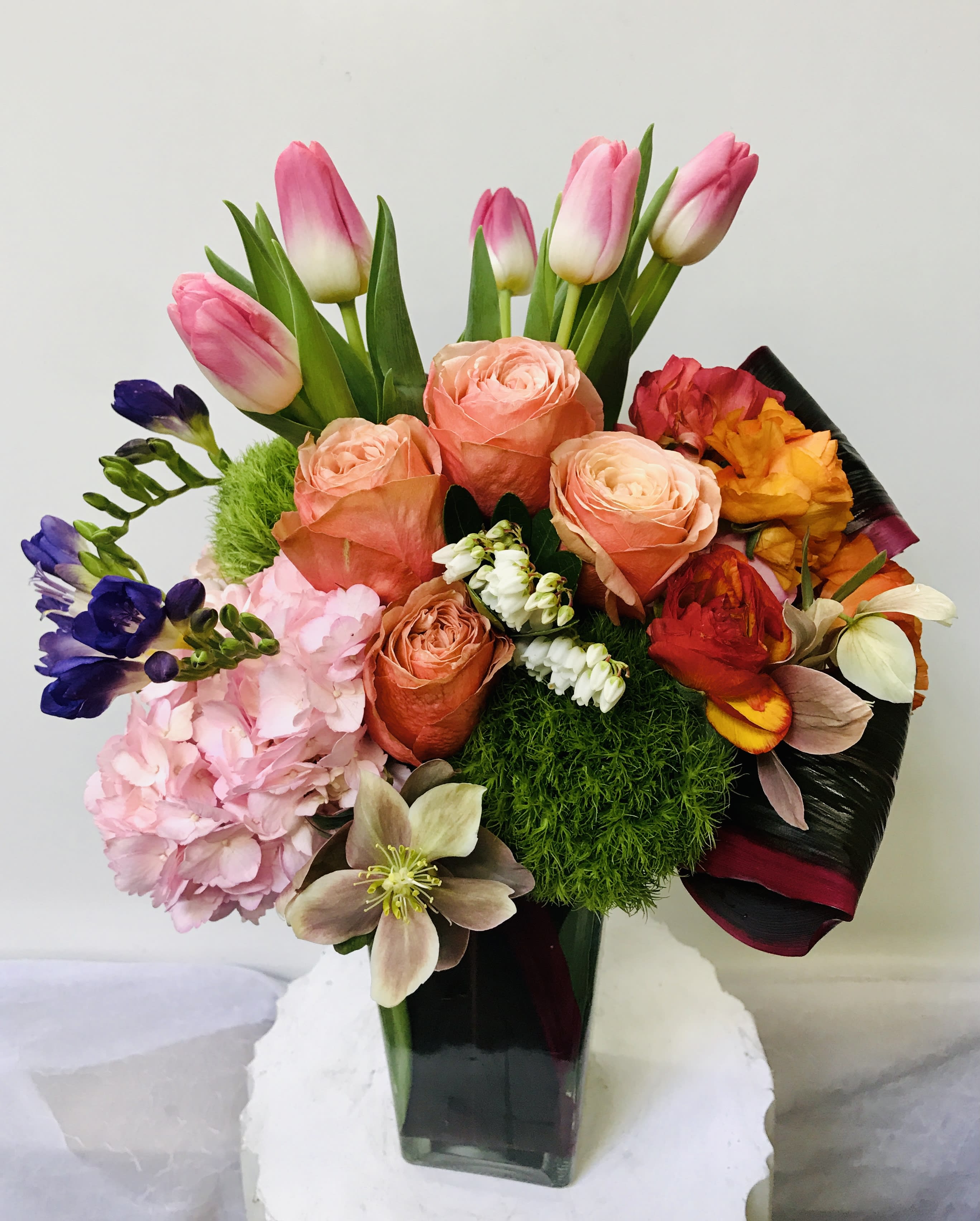 Mixed bouquet of pink tulips, peach roses, and colorful blooms in a glass vase