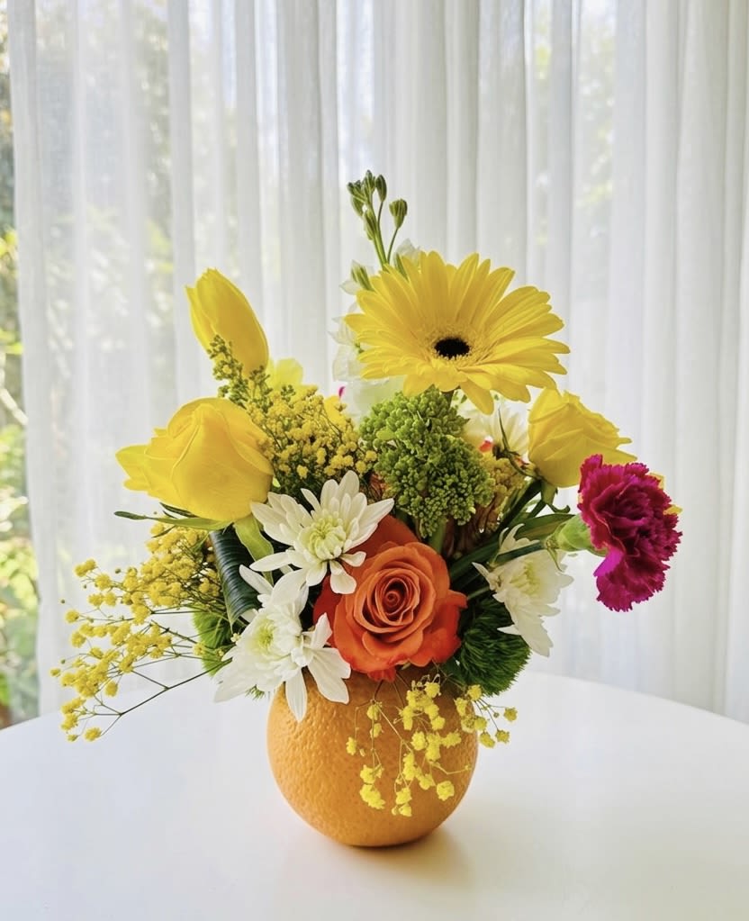Citrus Sunshine - Fresh Orange Floral Design - A bright, cheerful, and uniquely creative floral arrangement styled directly inside a real, fresh orange "vase." This delightful piece features a striking orange rose, a bold yellow gerbera daisy, and yellow roses, beautifully accented with white daisy chrysanthemums, a magenta carnation, lime-green trick dianthus, and airy yellow mimosa fillers.
