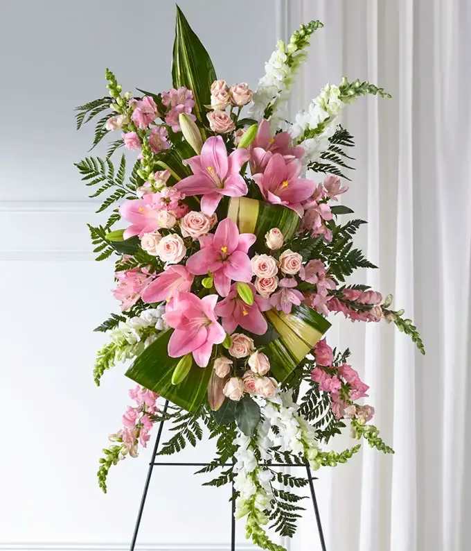 Blush of Grace Standing Spray - A graceful standing spray designed in soft pink and crisp white blooms to express love, compassion, and heartfelt remembrance. Featuring an elegant blend of premium flowers such as lilies, roses, chrysanthemums, pink spray roses, carnations, snapdragons, and seasonal greenery, this standing tribute creates a delicate and comforting display. Arranged on a standing easel, the soft pink and white palette symbolizes peace, admiration, grace, and everlasting affection — offering a beautiful way to honor and celebrate a cherished life.