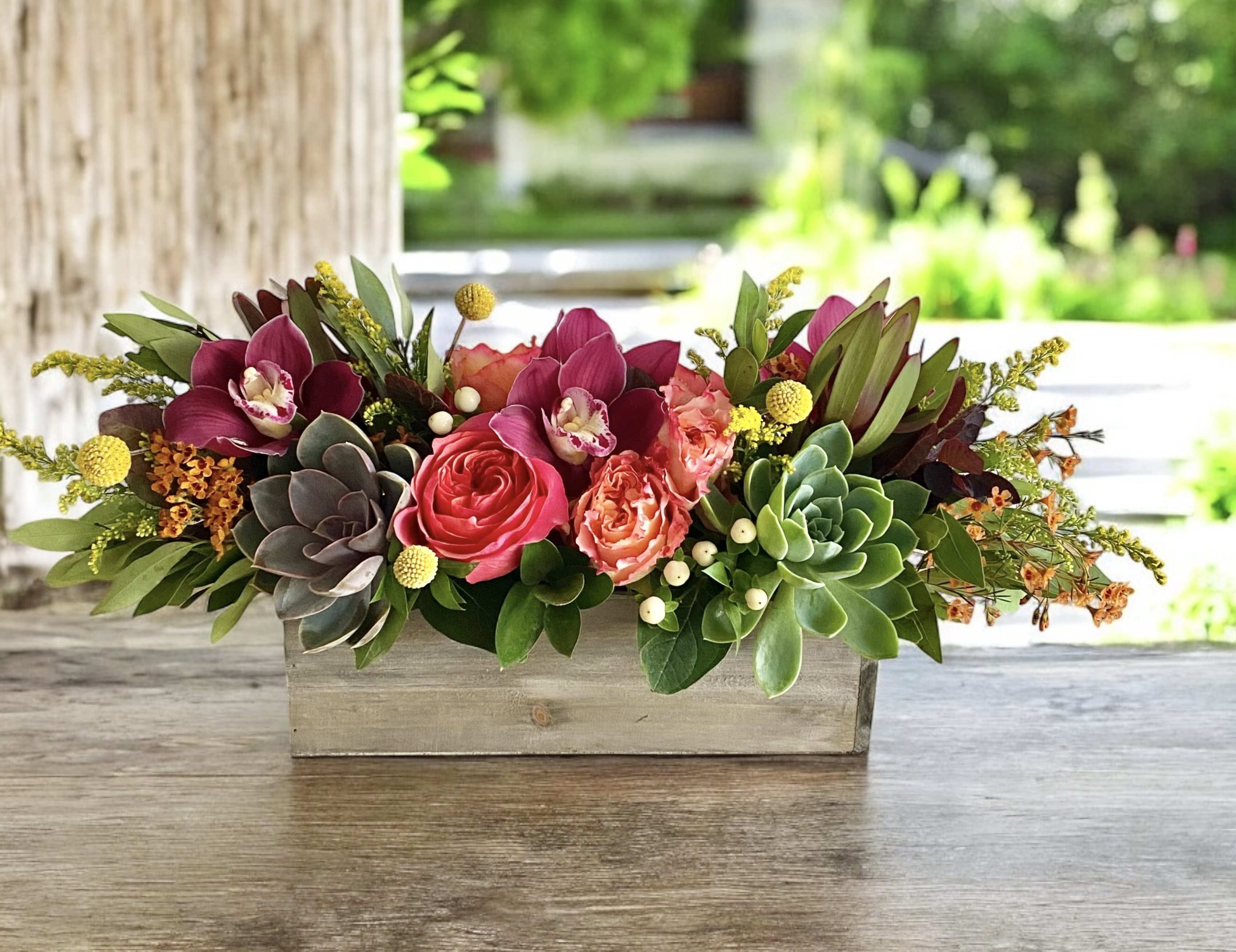 Low floral centerpiece in a rectangular wooden box with pink and burgundy blooms