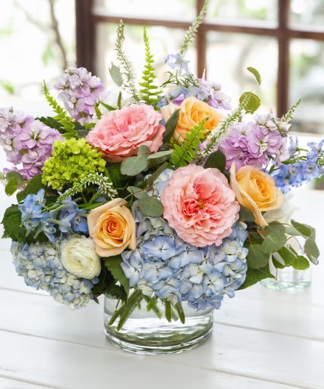 Pastel bouquet of roses, hydrangeas, and purple blooms in a glass vase
