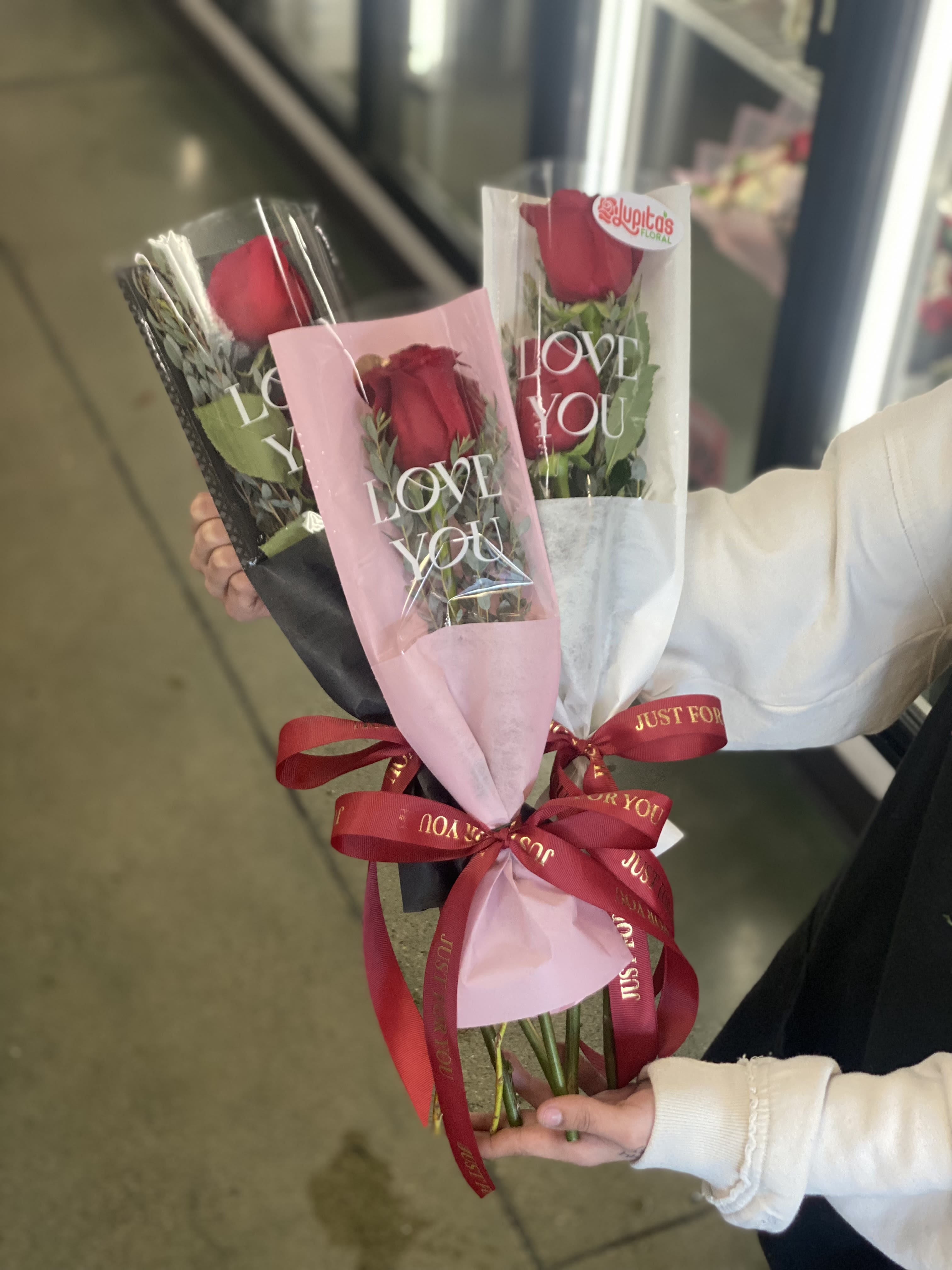 Three wrapped red rose bouquets with ribbons and "LOVE YOU" sleeves
