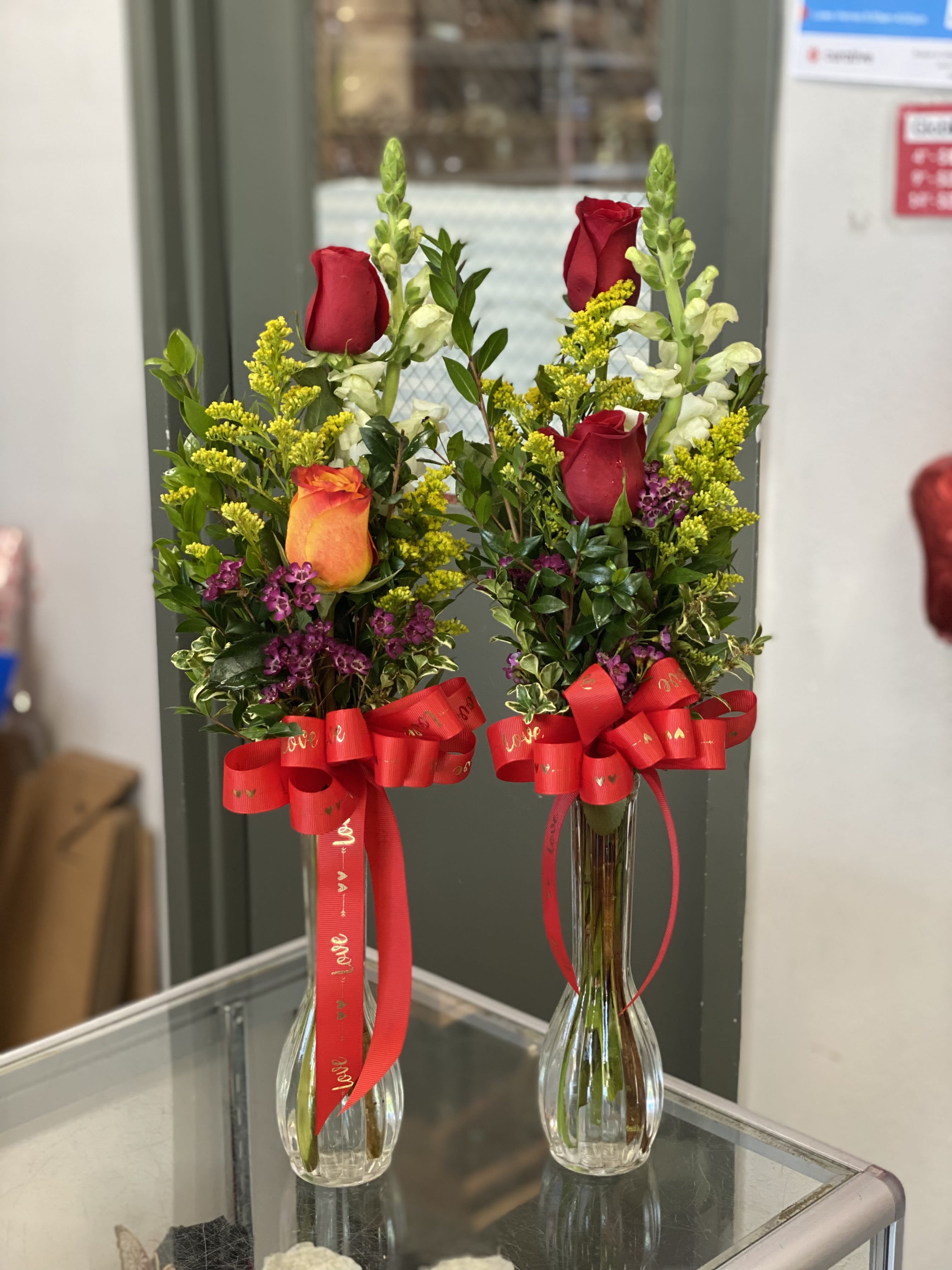 Two rose arrangements in clear glass vases with red ribbons