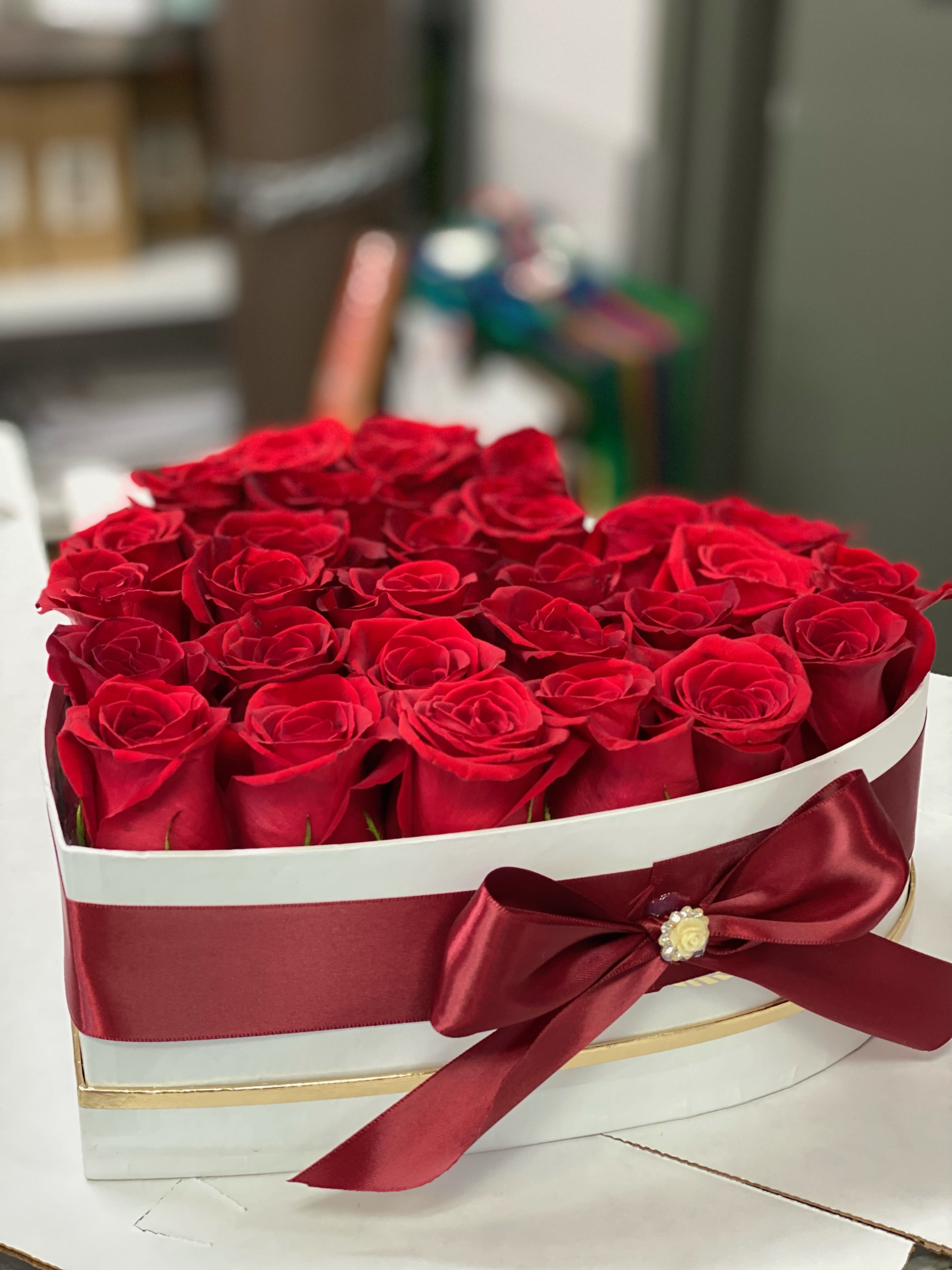 Heart-shaped box filled with red roses and a burgundy ribbon