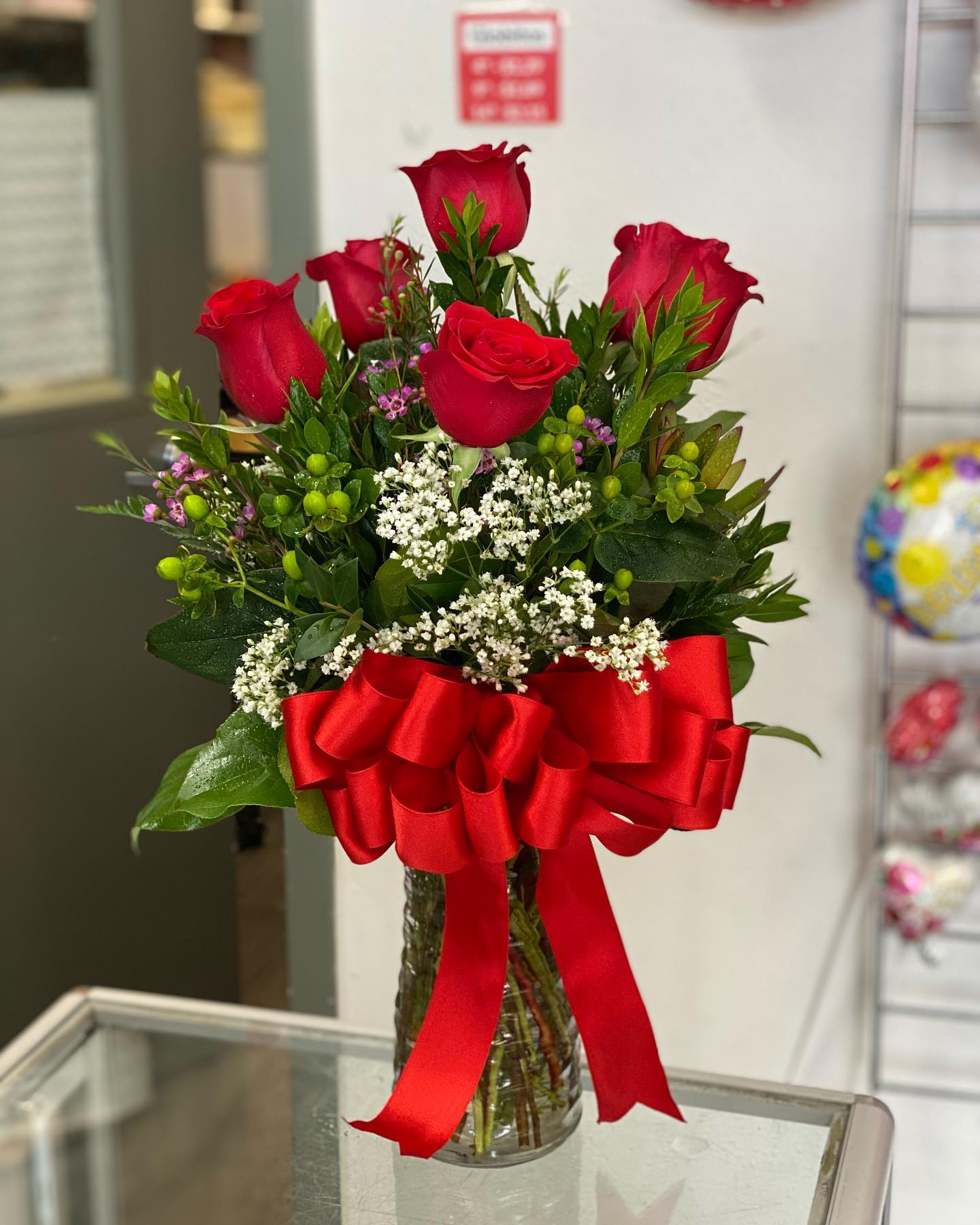 Red roses in a clear glass vase with a large red ribbon