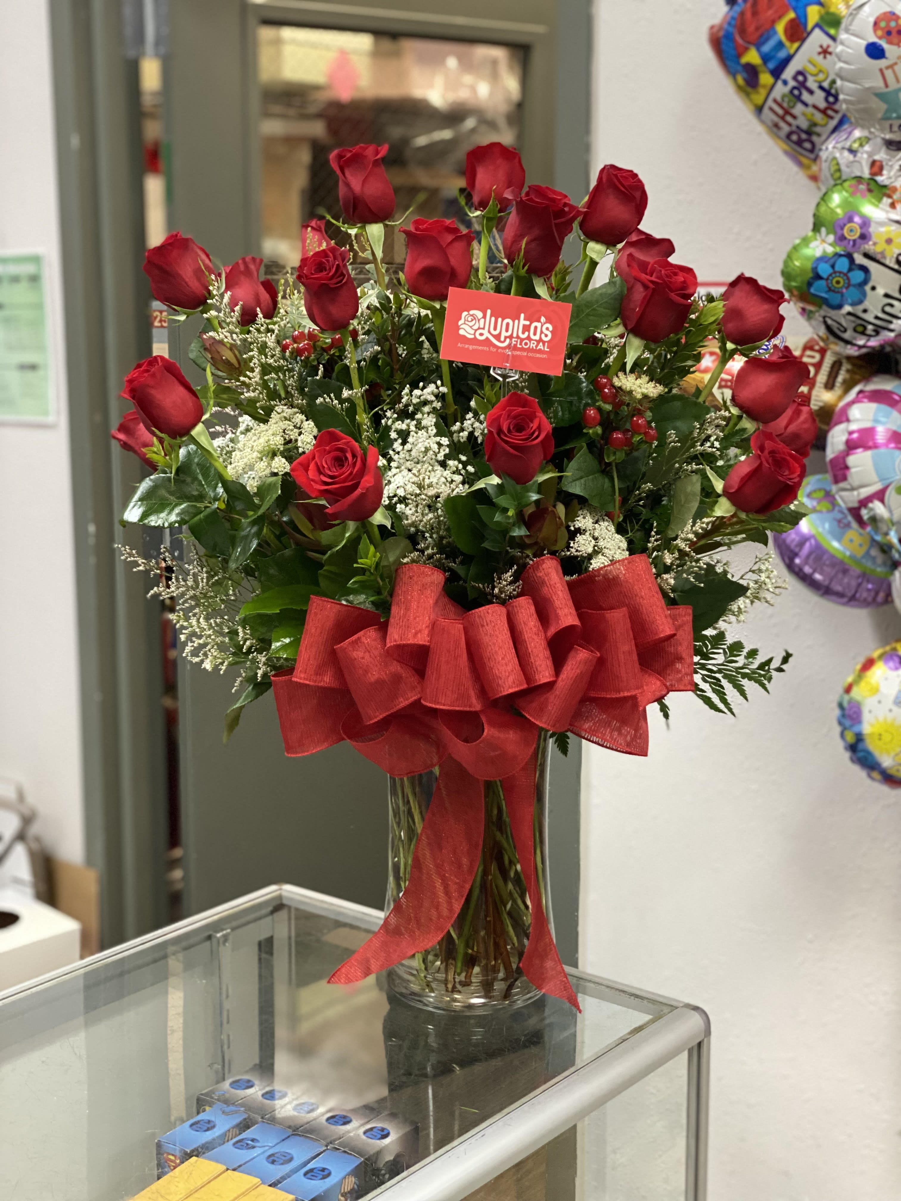 Red roses arranged in a clear glass vase with a large red bow