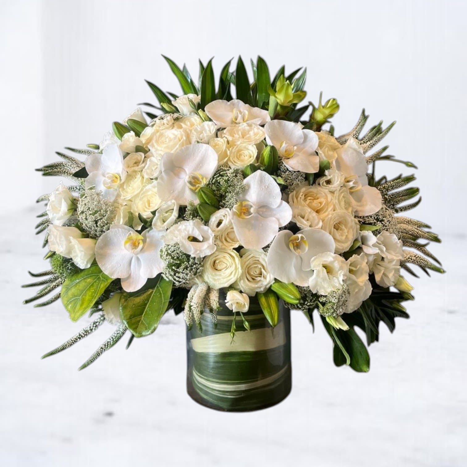 Sanctuary Elegance - Graceful and refined, the Sanctuary Elegance is a modern tribute that radiates peace, purity, and remembrance. This luxurious sympathy arrangement features white phalaenopsis orchids, roses, lisianthus, veronica, and queen anne’s lace, all artfully layered with tropical greens for dramatic contrast. Designed as a standing floor piece, it’s perfect for funeral services, celebration of life ceremonies, or sending condolences to the home.  Crafted with care and available for delivery to funeral homes and churches in Houston, Magnolia, Montgomery, The Woodlands, Conroe, and surrounding areas.