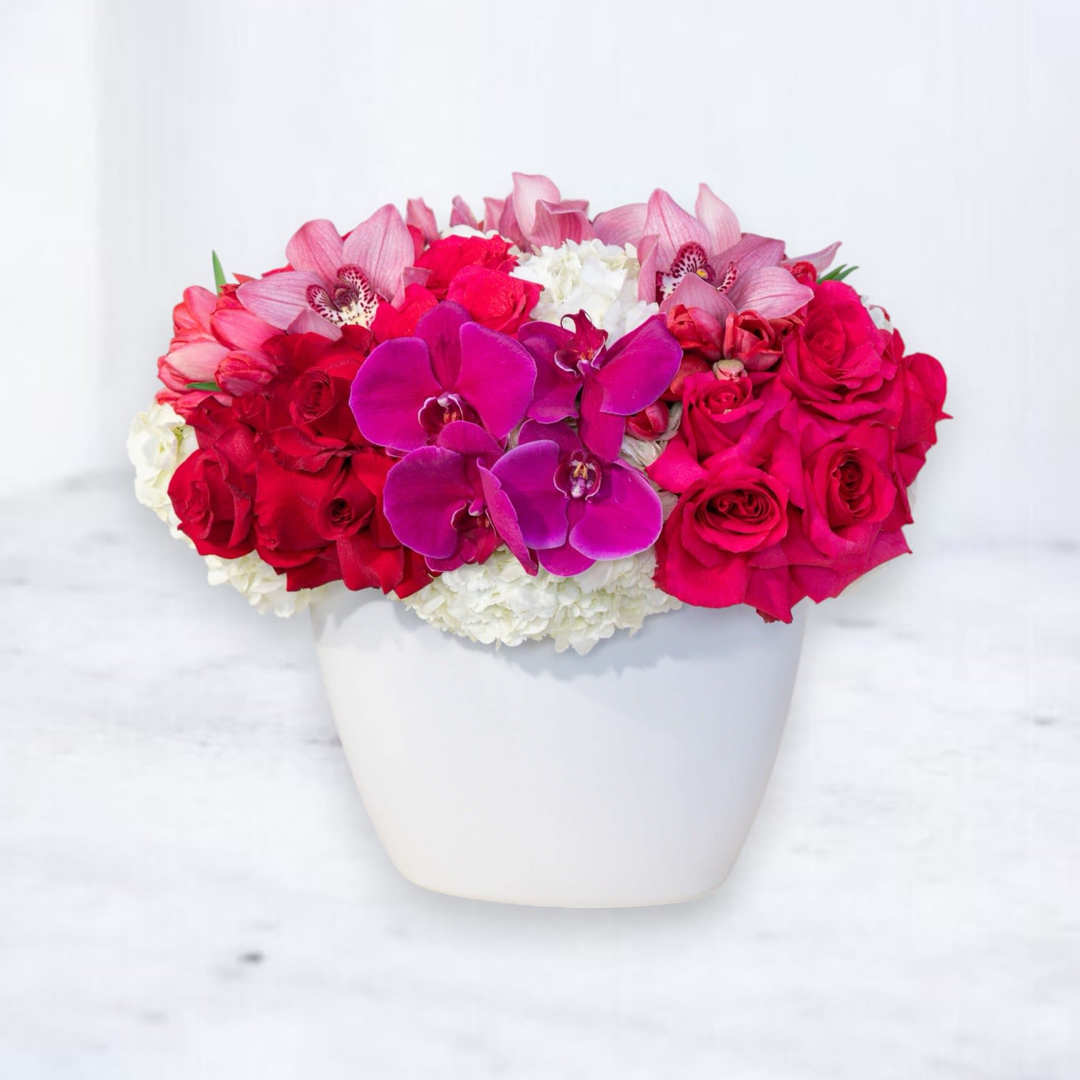 Passion Bloom Luxe - Elevate any occasion with the Passion Bloom Luxe, a breathtaking floral arrangement that radiates elegance and charm. Featuring vibrant magenta orchids, rich red roses, soft pink cymbidium orchids, and lush white hydrangeas, this luxurious bouquet is artfully arranged in a sleek white vase for a timeless and sophisticated look.  Perfect for birthdays, anniversaries, celebrations, or simply bringing beauty into someone’s day, the Passion Bloom Luxe is a statement of grace and refinement. Available for same-day delivery in Houston and surrounding areas, this exquisite arrangement adds a touch of luxury to every moment.    Orchid and rose floral arrangement for any occasion Elegant magenta and red flower bouquet with hydrangeas Same-day flower delivery in Houston for celebrations Sophisticated white vase floral arrangement with orchids and roses Premium floral gift for birthdays, anniversaries, and special moments
