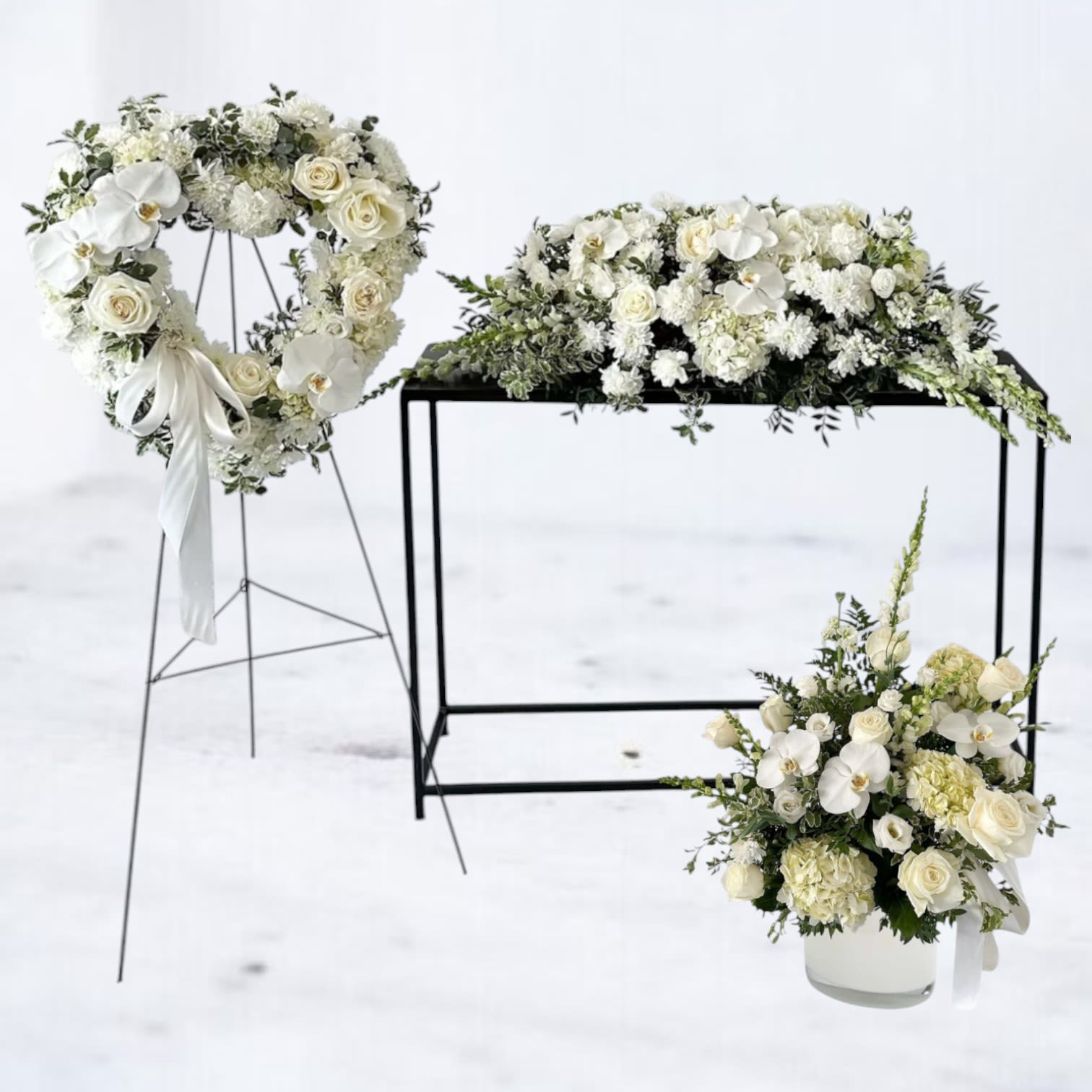 Serenity Remembrance - Honor a cherished life with the Serenity Remembrance Funeral Package, a graceful and heartfelt tribute. This elegant set includes a classic heart-shaped wreath symbolizing eternal love, a lush casket cover adorned with pure white roses, orchids, and hydrangeas, and a refined funeral basket offering peace and comfort. Each arrangement features a harmonious blend of soft, white blooms and lush greenery, evoking serenity and grace. Perfect for memorials, funerals, or celebration of life services, this package offers a timeless expression of sympathy.  The standard size arrangements feature elegant hydrangeas, carnations, and filler florals. For those seeking an elevated design, roses and Phalaenopsis orchids are available in upgraded sizes for a more luxurious and personalized tribute.