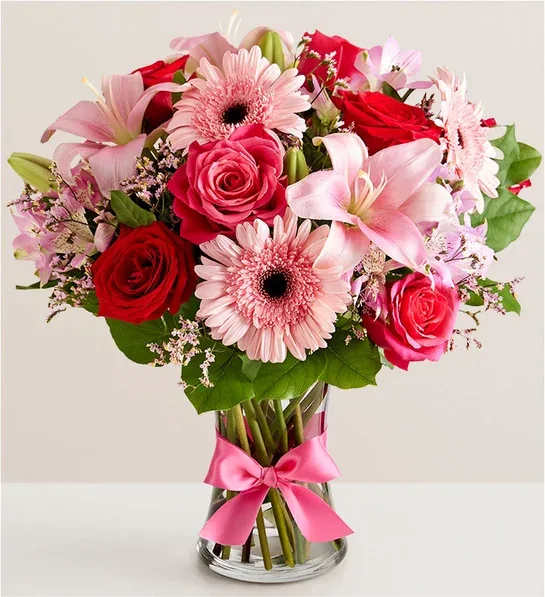 Pink and red mixed bouquet in a clear glass vase with a pink ribbon