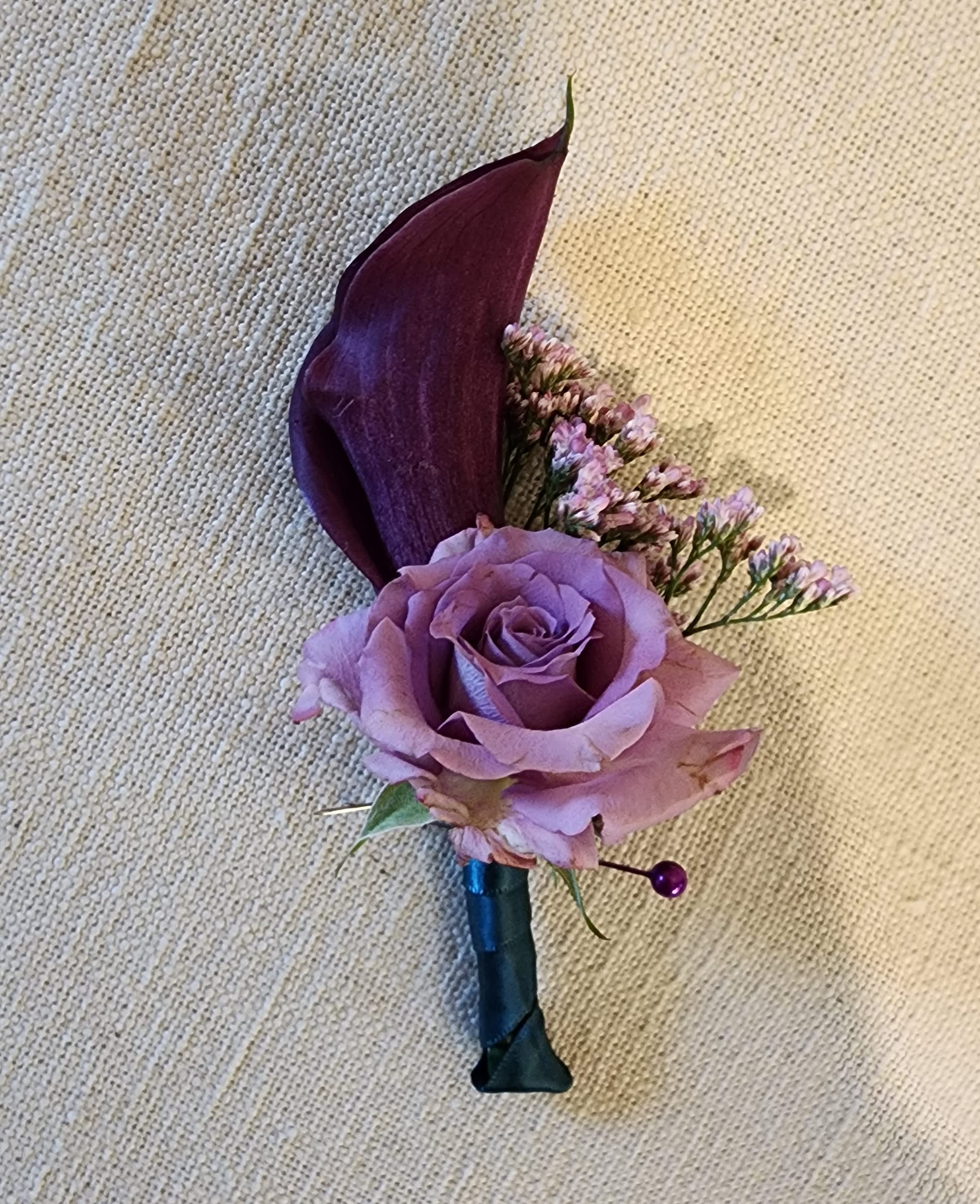 Purple rose boutonniere with a dark calla lily and small filler flowers