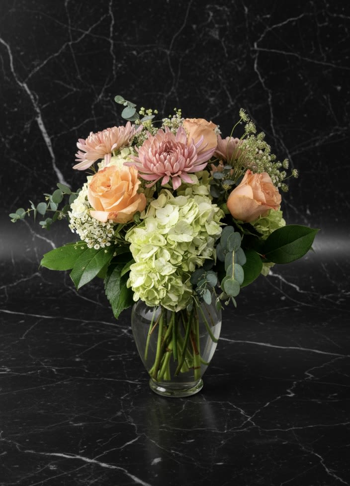Peach roses and pink blooms in a clear glass vase