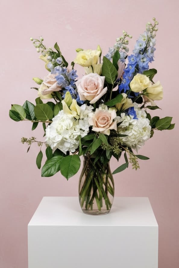 Mixed bouquet of pastel roses, hydrangeas, and blue delphinium in a glass vase