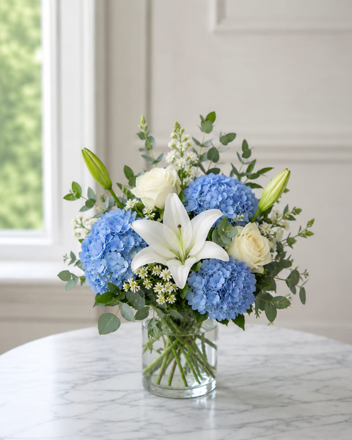 Ocean Breezes - Elegant arrangement featuring blue hydrangea, white roses, and white lilies for a classic look for any occasion. It is perfect for a beach house, river house, or any home in between.   Vase may vary based on availability.  A substitution notice will be sent with any floral changes.