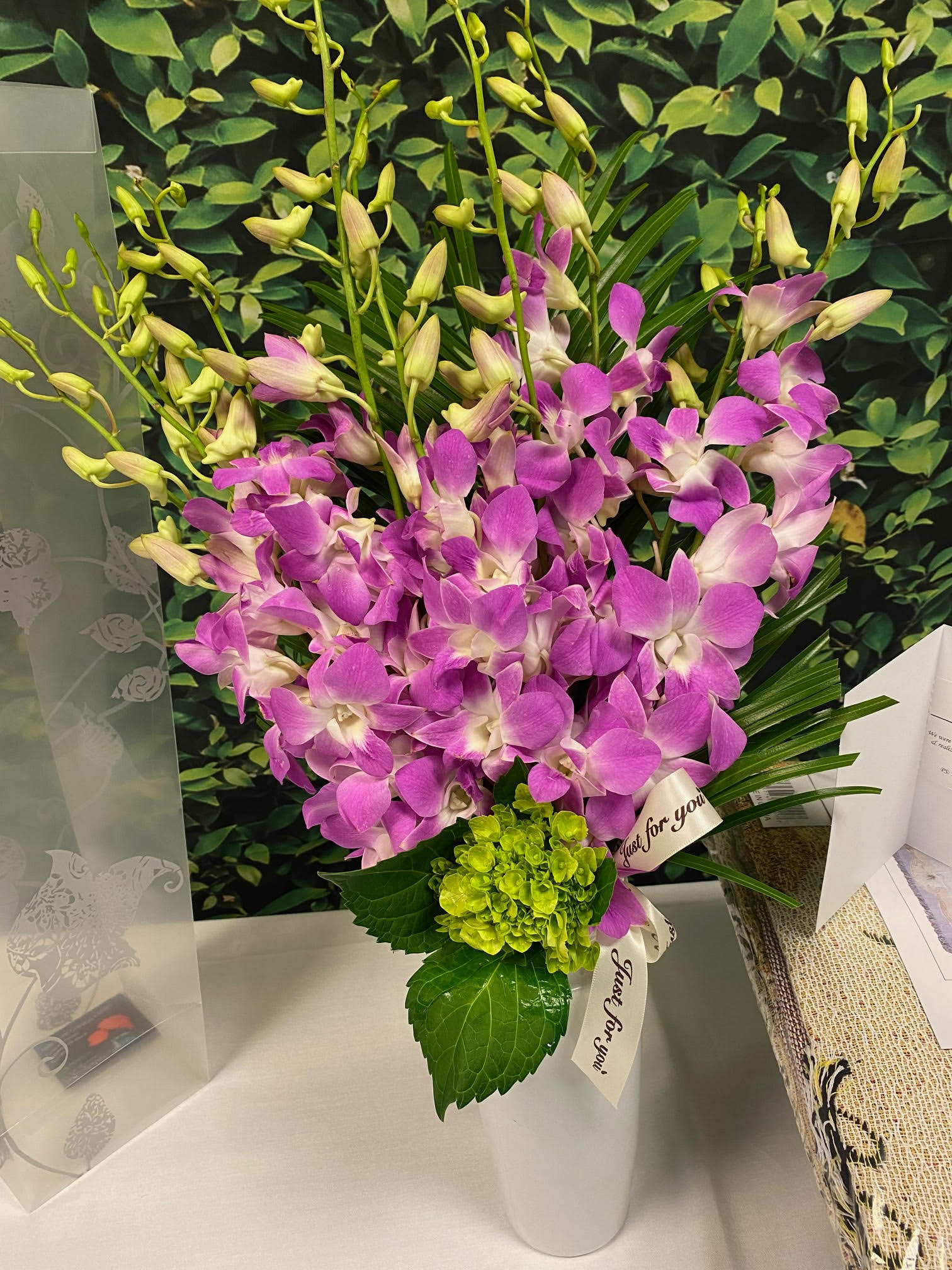 Purple orchids arranged in a white vase with a green hydrangea accent