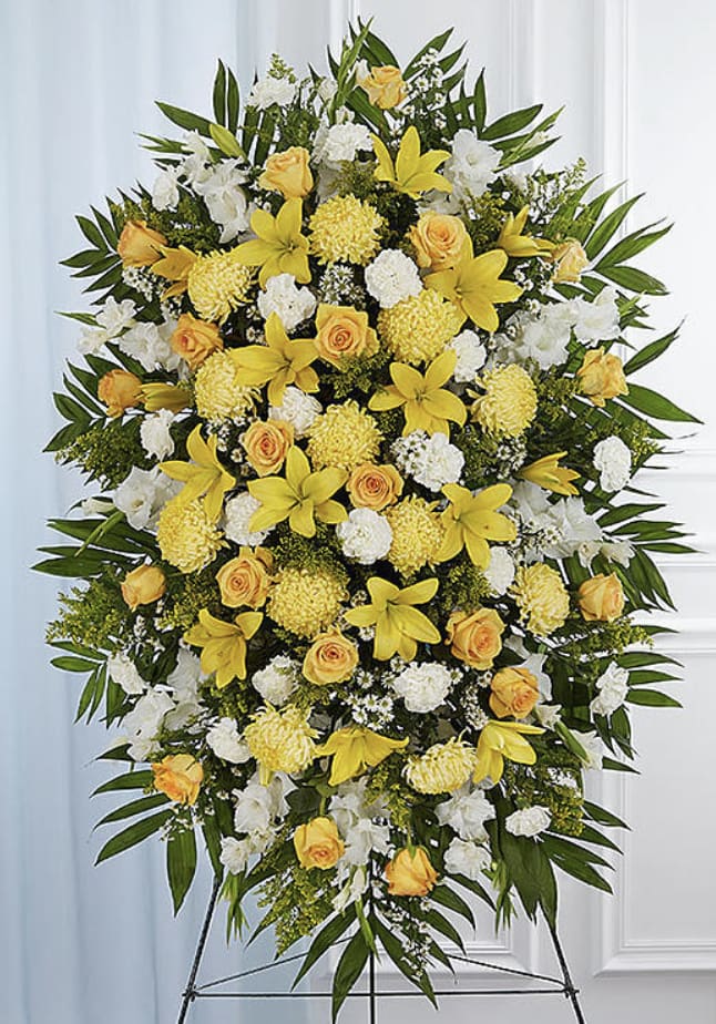 Eternal Light Standing Spray - A radiant yellow and white standing spray designed to bring warmth, comfort, and peaceful remembrance. This elegant tribute features a graceful blend of sunny yellow roses, carnations, paired with elegant lilies, chrysanthemums, and spray roses, beautifully accented with lush seasonal greenery. Arranged on a standing easel, the uplifting color palette symbolizes hope, peace, friendship, and a life filled with light and love. Its bright yet elegant design offers a heartfelt expression of sympathy while celebrating cherished memories with grace and beauty.