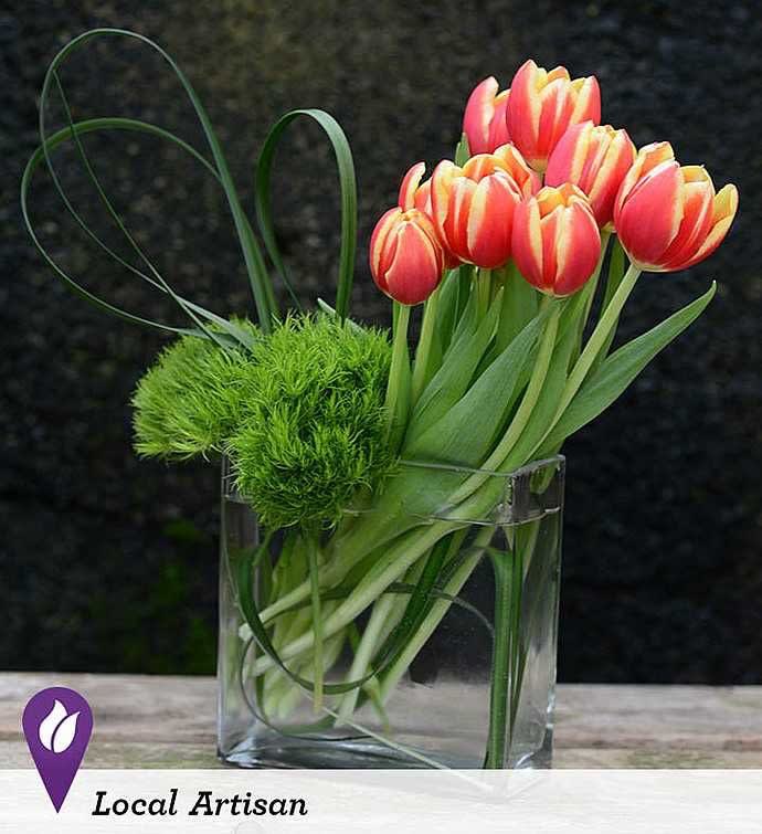 Pink and yellow tulips in a clear glass vase with green decorative accents