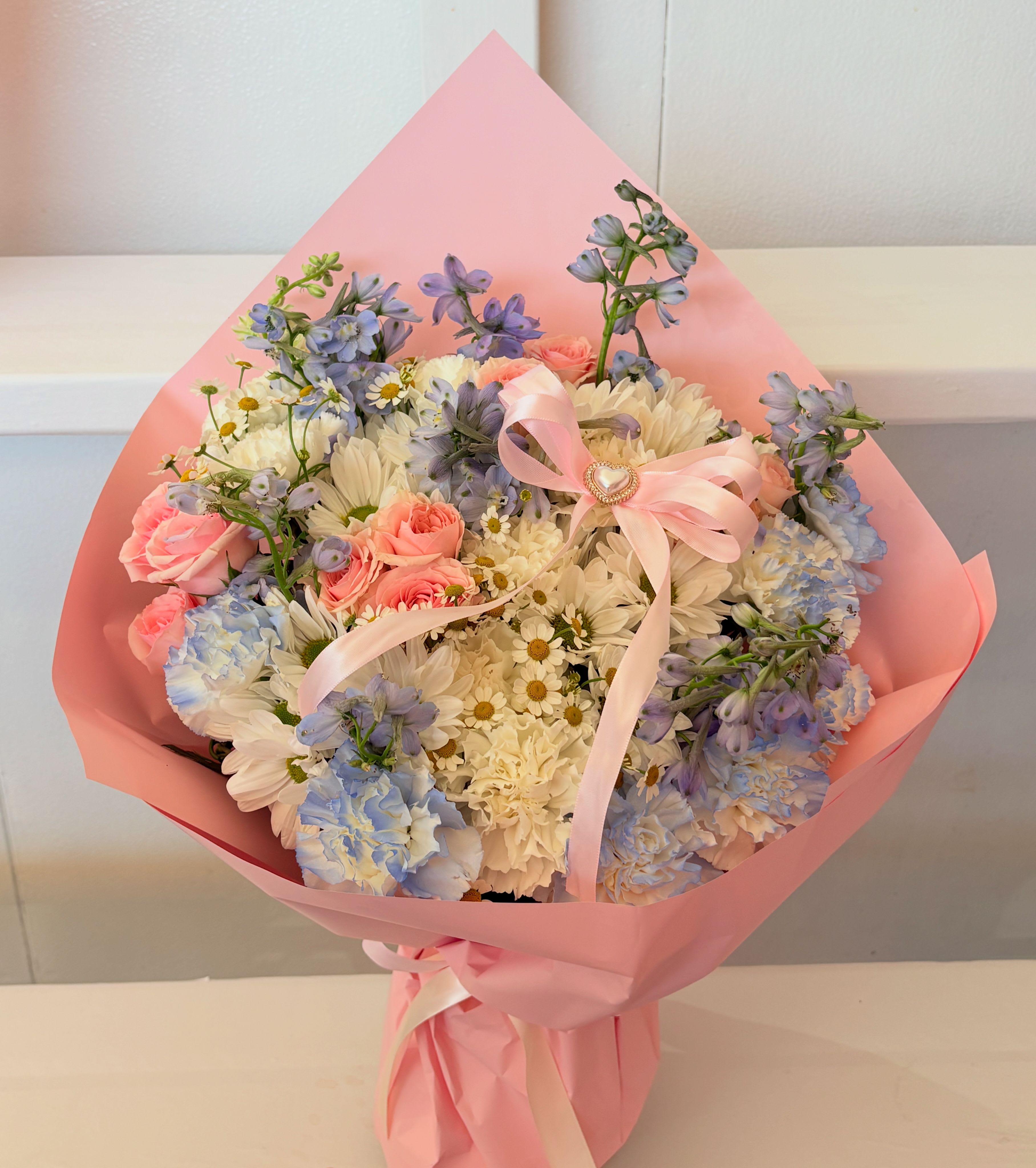 Bouquet of pink roses, white daisies, and blue flowers wrapped in pink paper
