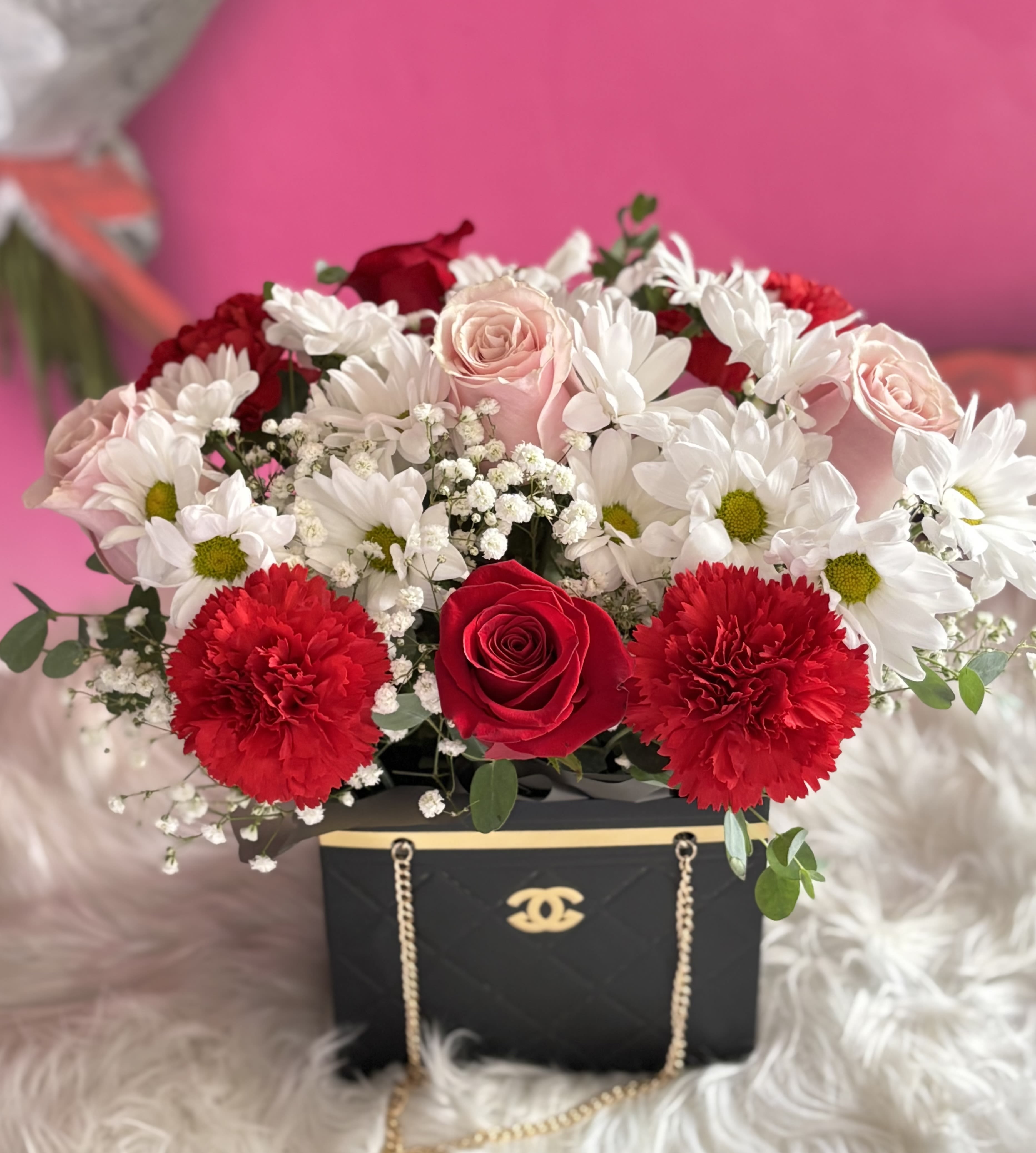Red, pink, and white flowers arranged in a black gift box with gold chain detail