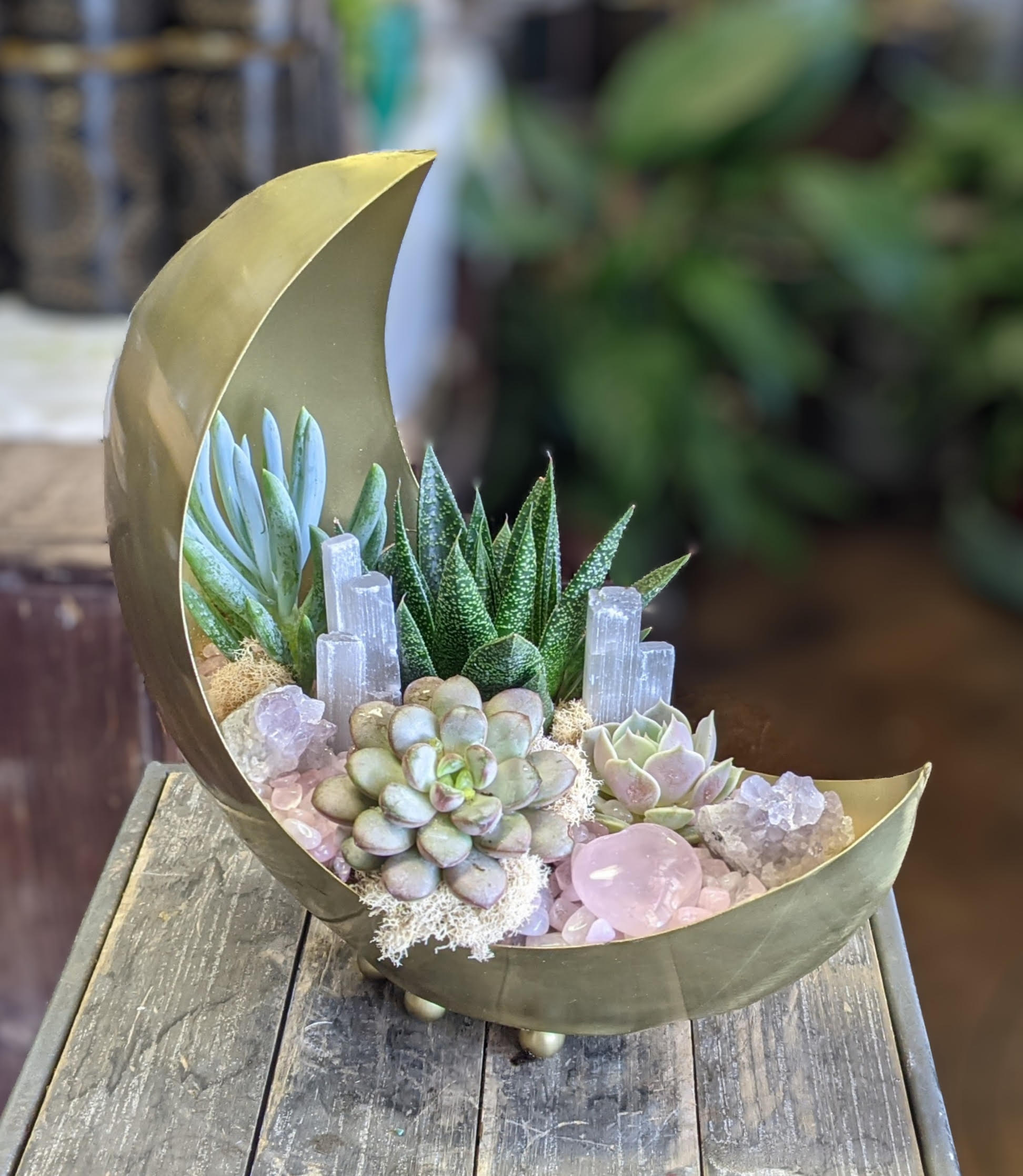 Succulent arrangement in a crescent-shaped gold container with crystal accents
