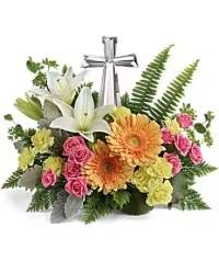 Faith &amp; Remembrance - A heartfelt sympathy table arrangement thoughtfully designed around a keepsake crystal cross. This elegant tribute features white lilies, orange gerberas, pink spray roses, and yellow mini carnations, beautifully accented with fresh greenery for a full and balanced display.  Perfect for memorial services or as a lasting tribute, the combination of vibrant blooms with the crystal cross offers a meaningful expression of faith, remembrance, and comfort to honor a cherished life.