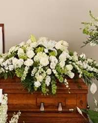 Heavenly White Tribute Casket Spray - A luxurious and elegant all-white casket spray designed to honor a cherished life with grace and beauty. This premium arrangement features white oriental lilies, white roses, white stock or snapdragons, bells of Ireland, white carnations, mini carnations, and white hydrangeas, all thoughtfully arranged with fresh mixed greenery for a full and flowing presentation.  The timeless all-white palette symbolizes peace, purity, and eternal love, creating a dignified and heartfelt tribute. Designed to rest gracefully across the casket, this arrangement offers a beautiful and respectful expression of sympathy and remembrance.