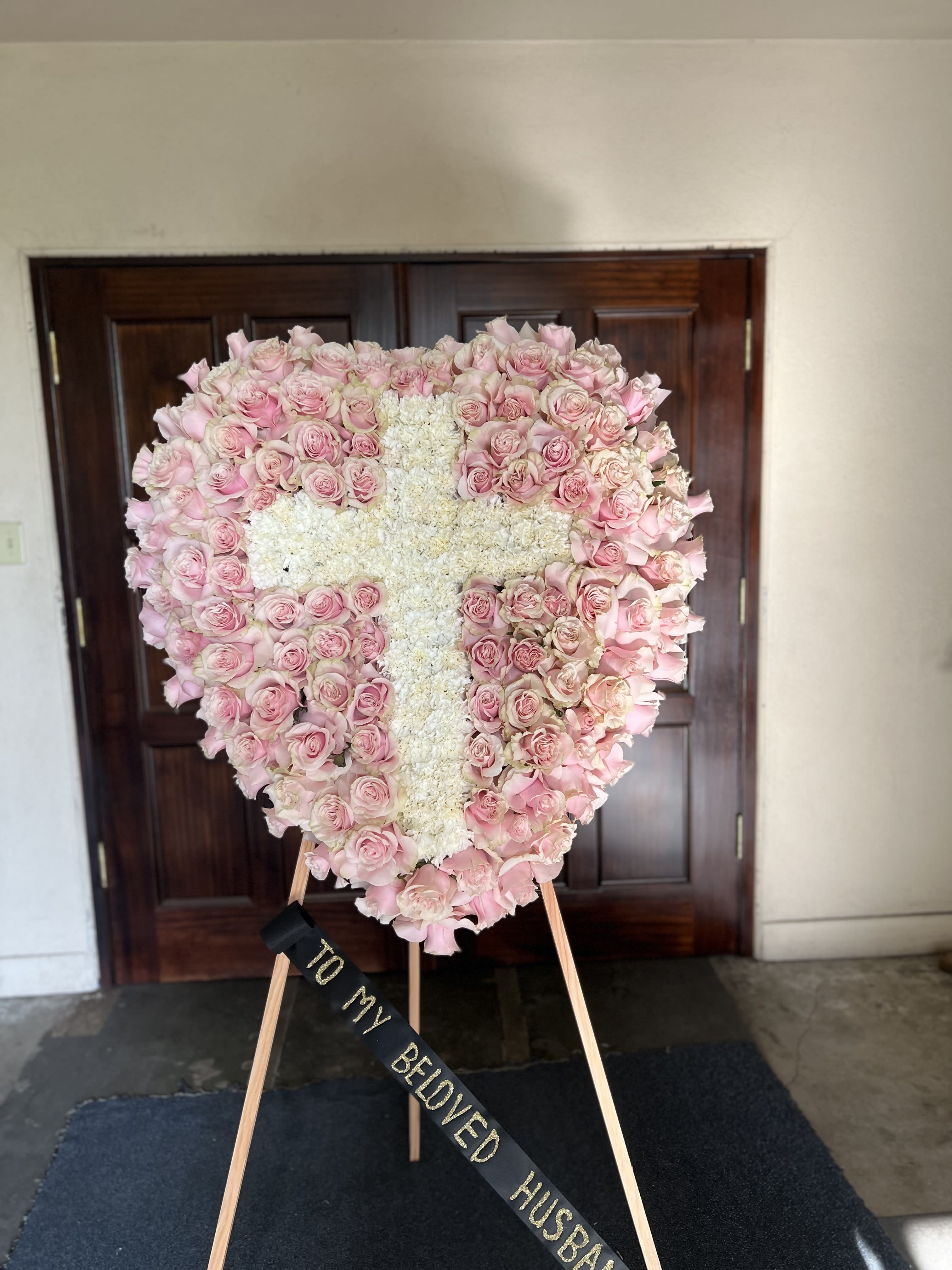 Heart-shaped pink rose wreath with a white floral cross on an easel