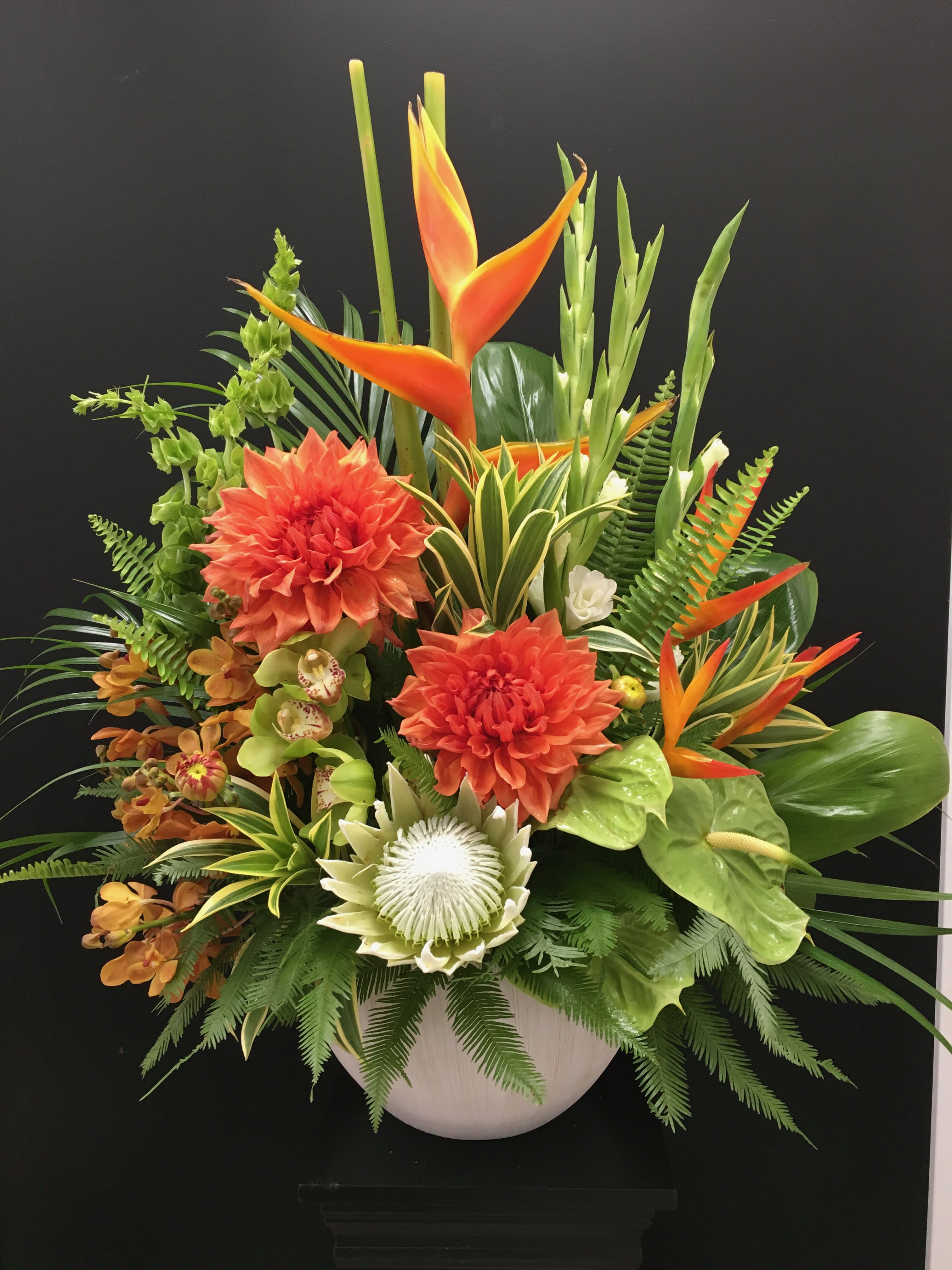 Tropical floral arrangement with orange blooms in a white vase