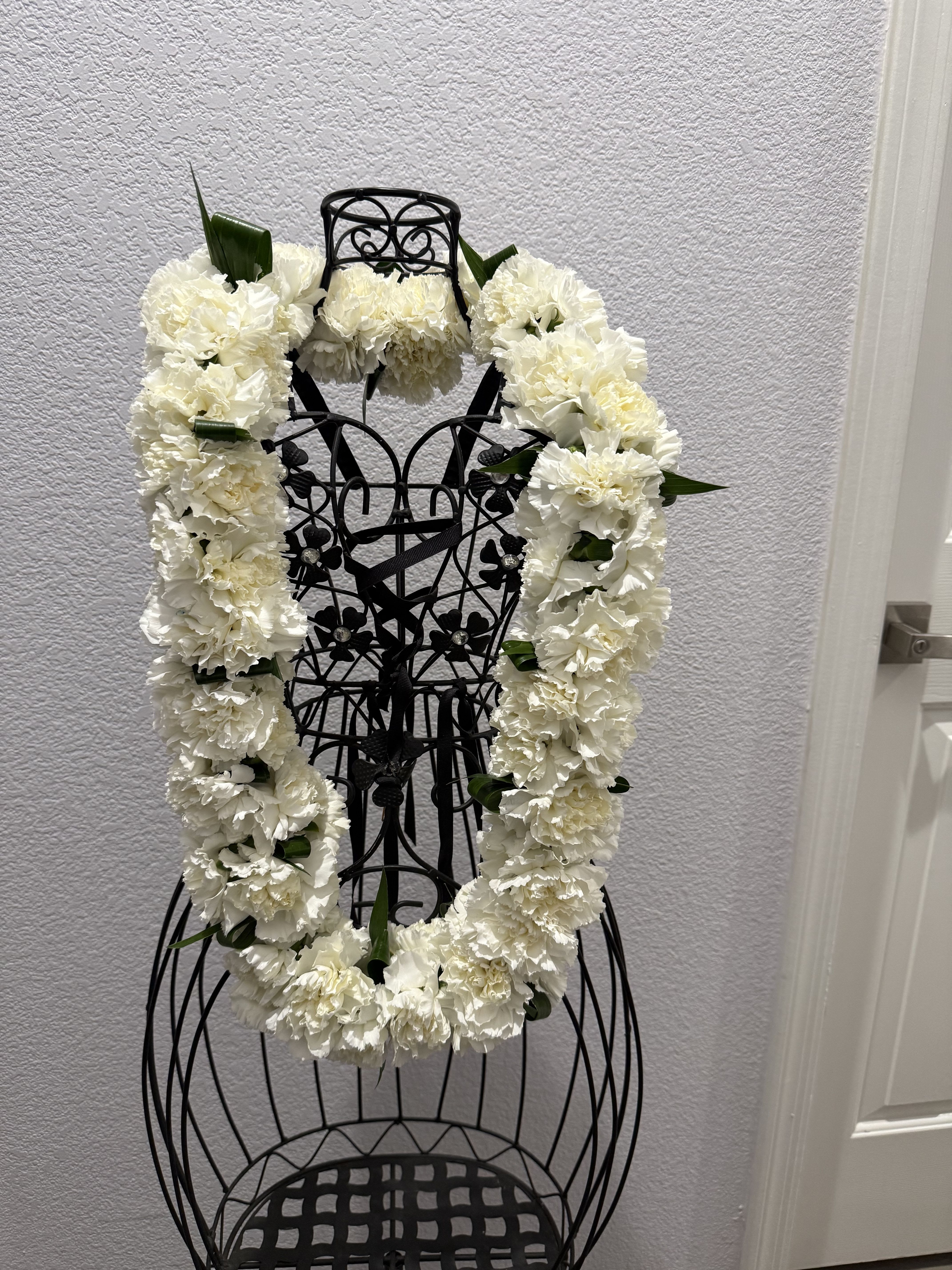 Carnation lei - A full, ceremonial white carnation lei creates an immediate sense of reverence and grace - perfect as a memorial tribute, graduation presentation, or formal wedding accent. The dense, ruffled carnations form a continuous, cloud-like circle that reads clean and classic from a distance, so the person you're honoring will feel seen and respected.  Each lei is made of tightly clustered white carnations with small touches of green foliage woven through for subtle contrast, dimensions and exact stem counts vary by size selected, and the piece is designed for short-term display   Choose this arrangement when you want a formal, display-ready tribute that communicates respect and care - whether for a funeral service, graduation ceremony, or elegant wedding décor. Please note these are fresh flowers best enjoyed on the day of the event; contact us for delivery timing and sizing options to ensure the lei arrives ready to display.