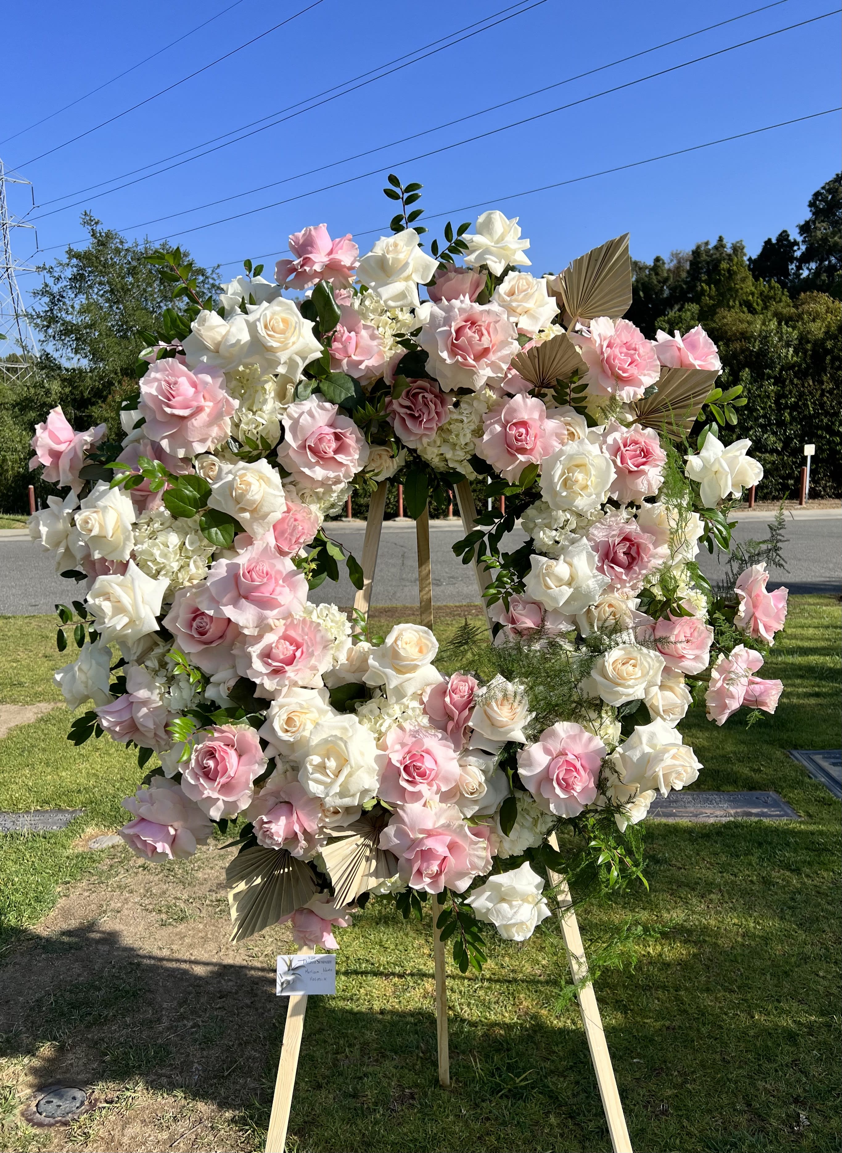 Large pink and white rose wreath on a wooden stand outdoors