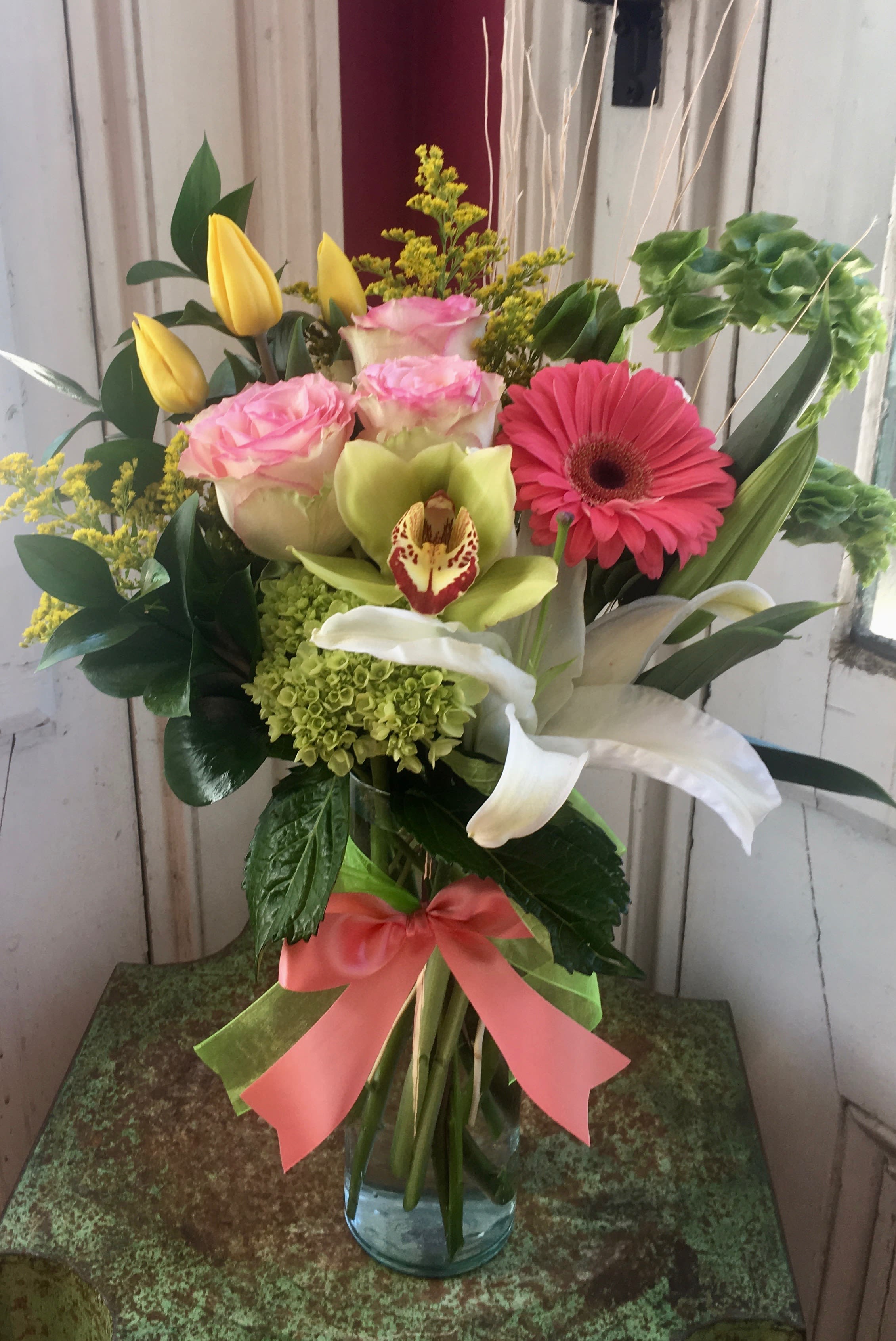 Mixed bouquet in a glass vase with pink roses, yellow tulips, and a pink gerbera daisy