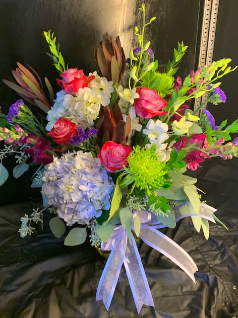 Colorful bouquet of roses, hydrangeas, and orchids with a ribbon bow