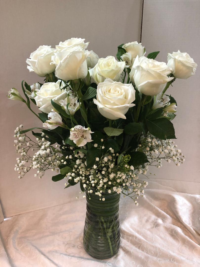 White roses and small white filler flowers in a tall glass vase