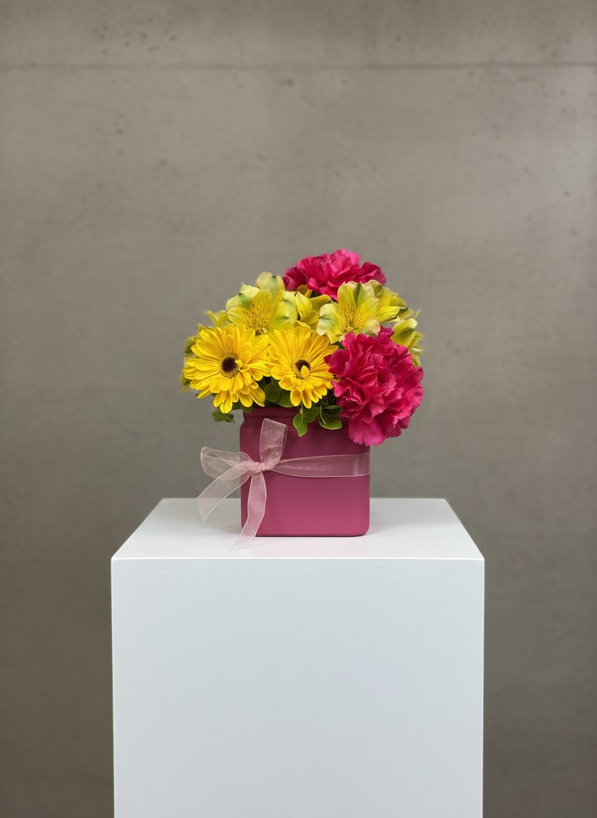 Pink and yellow flowers arranged in a magenta box with a ribbon
