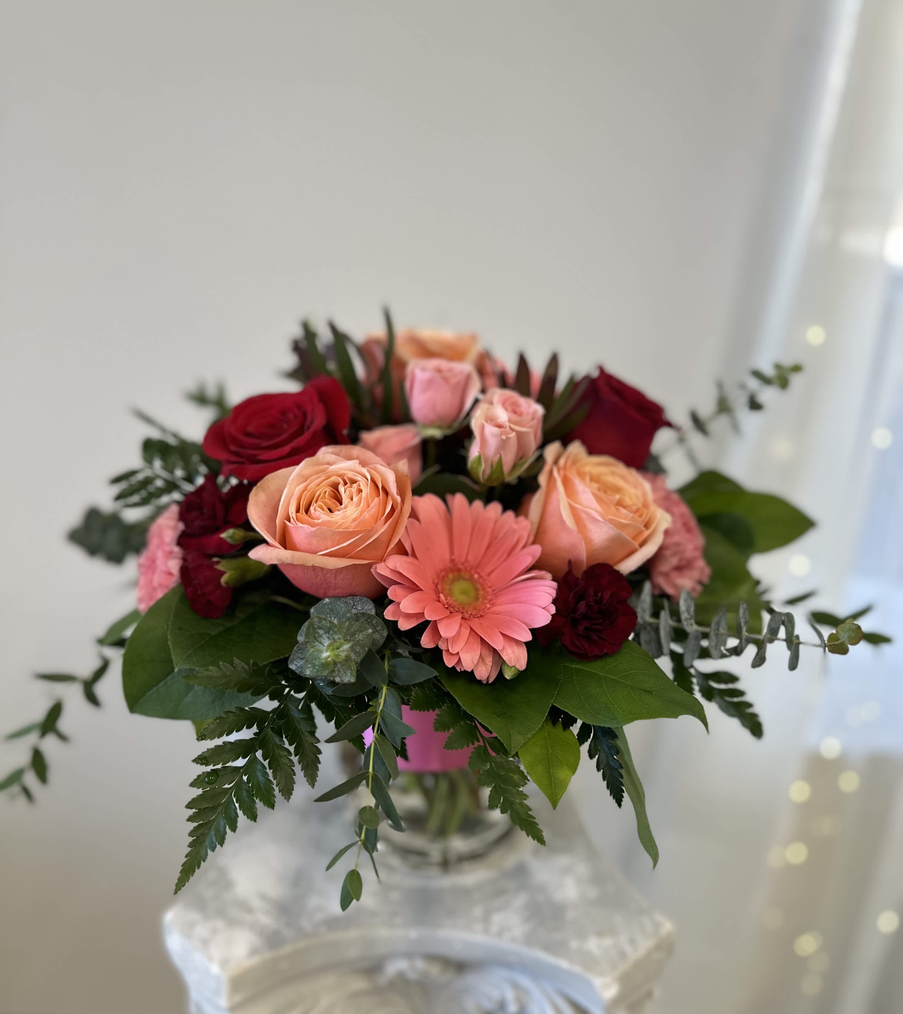 Bouquet of peach and red roses with a pink gerbera daisy in a glass vase