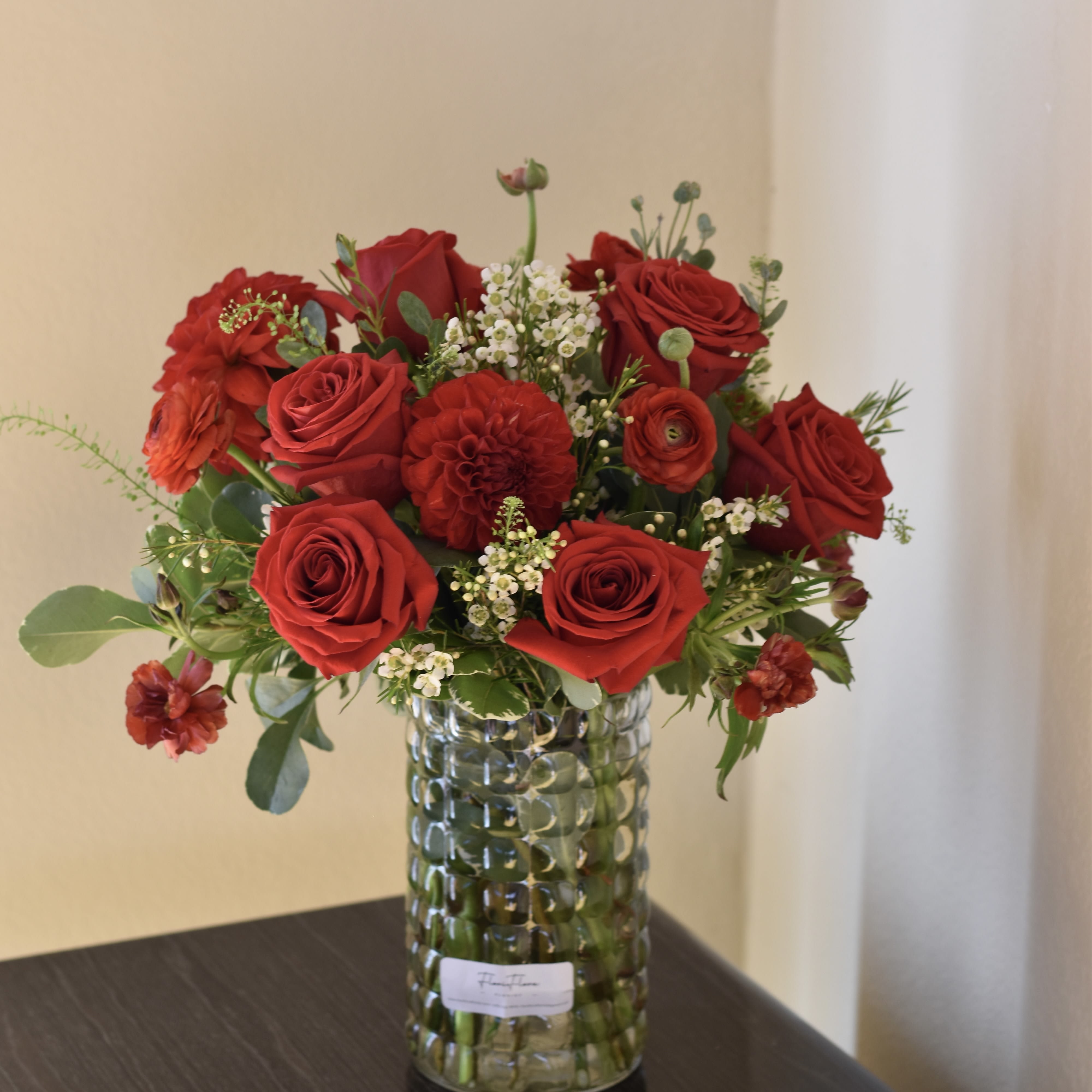 Heartbeat of Love - "Heartbeat of Love" is a stunning and passionate flower arrangement that embodies the essence of deep, unwavering affection. This arrangement is a symphony of rich red hues, featuring the most romantic and symbolic flowers.  At the heart of this creation are the classic red roses, their velvety petals symbolizing love and devotion. Surrounding them are vibrant red ranunculuses, known for their lush, layered blooms that add depth and texture to the arrangement. Completing the ensemble are striking red dahlias, with their intricate, bold petals, representing inner strength and the beauty of everlasting love.  The combination of these three flowers creates a powerful visual impact, making "Heartbeat of Love" a perfect expression of passionate emotions. Whether for a special occasion or as a grand gesture of love, this arrangement is sure to leave a lasting impression, just like the beat of a loving heart.