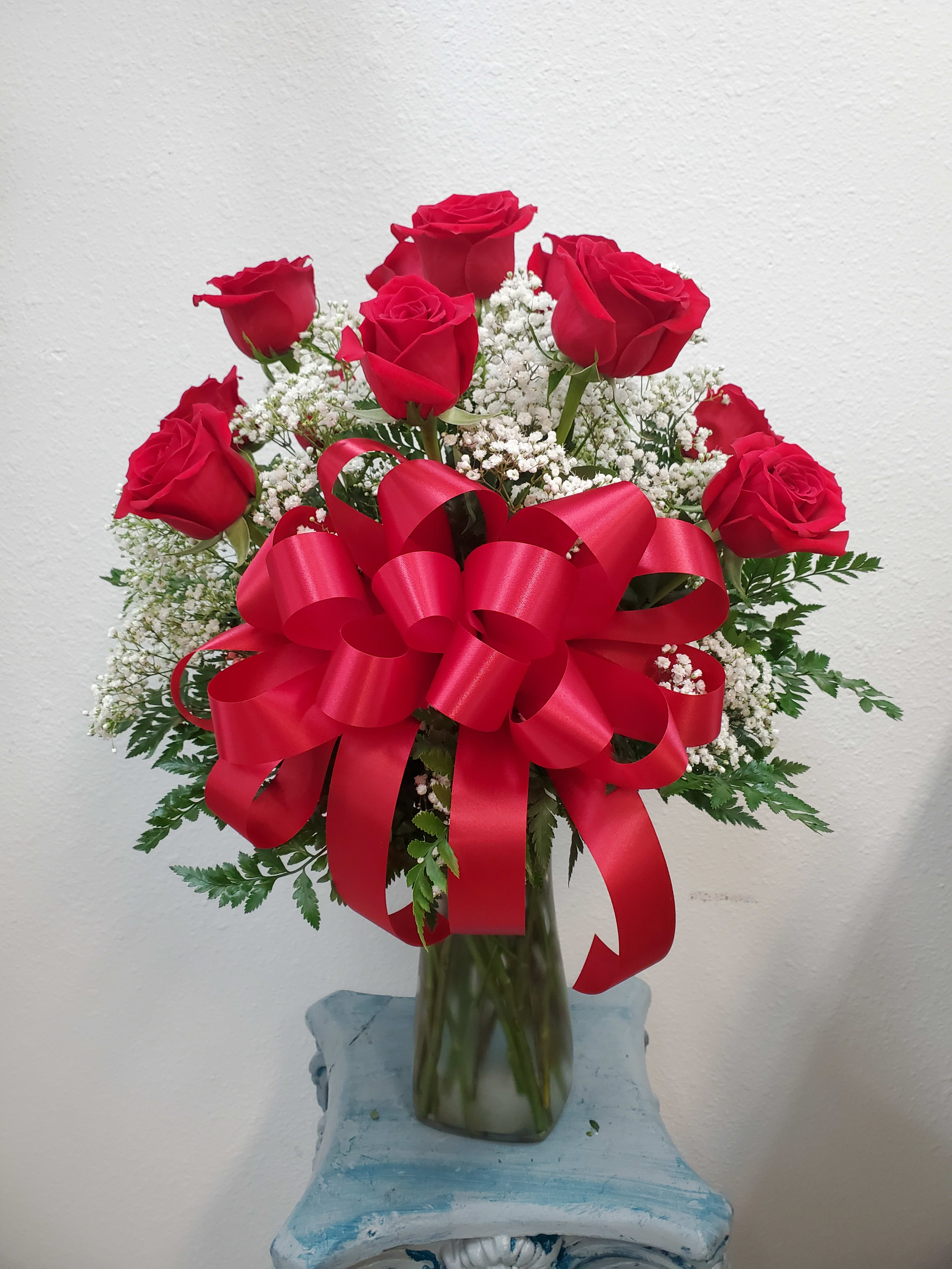 Bouquet of red roses with baby's breath in a glass vase and red ribbon