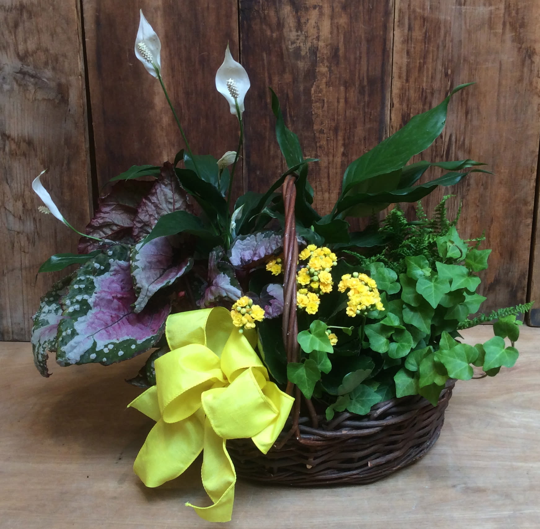 Basket arrangement with white calla lilies, yellow flowers, and a bright ribbon