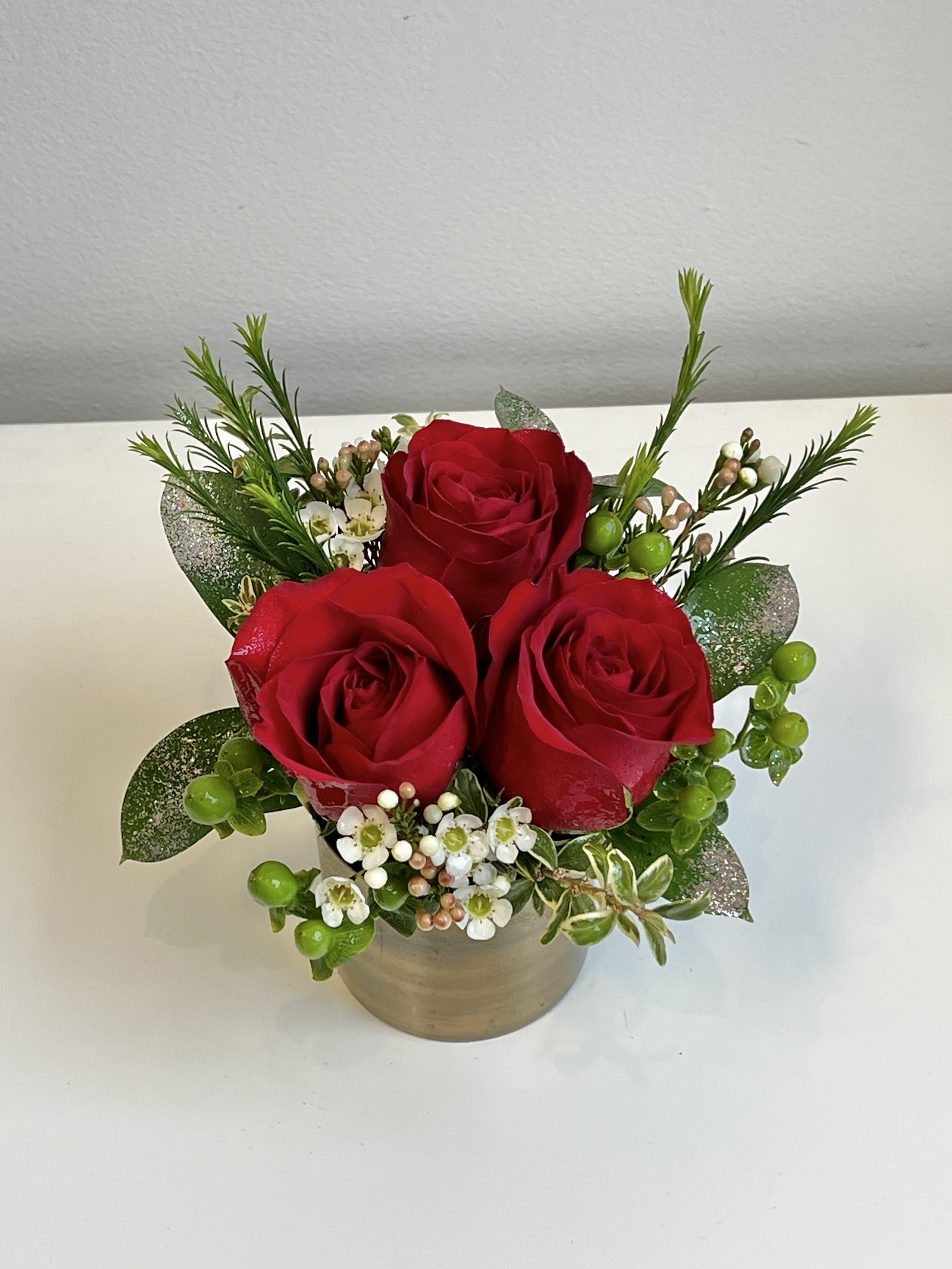 Three red roses in a small beige pot with white filler flowers