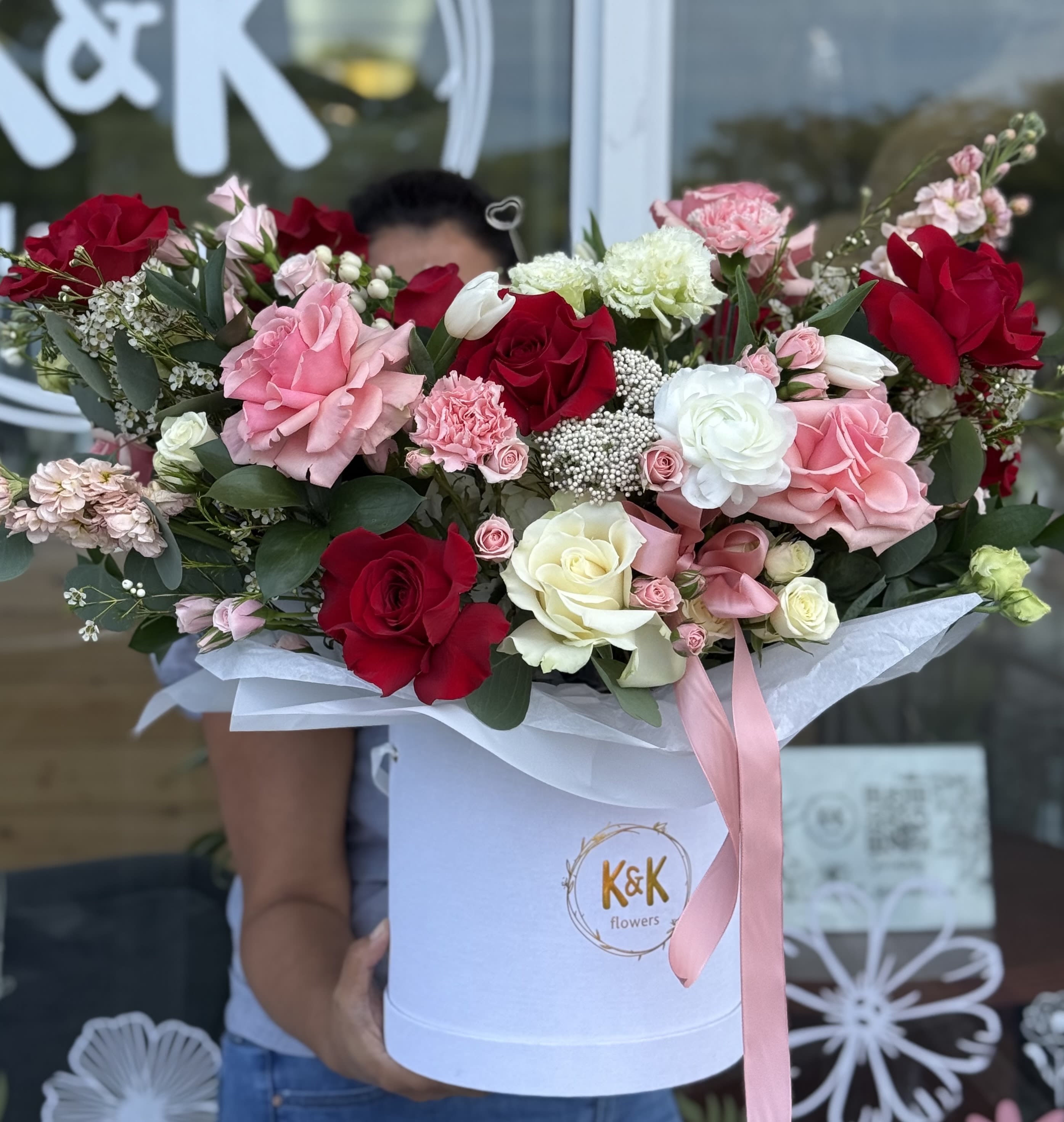 Large bouquet of red, pink, and white roses in a white hatbox with a pink ribbon.