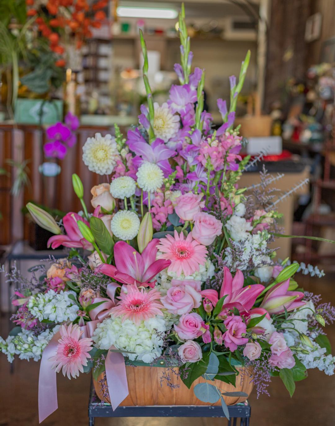 Large pastel flower arrangement with pink lilies, roses, and gerbera daisies in a wooden basket