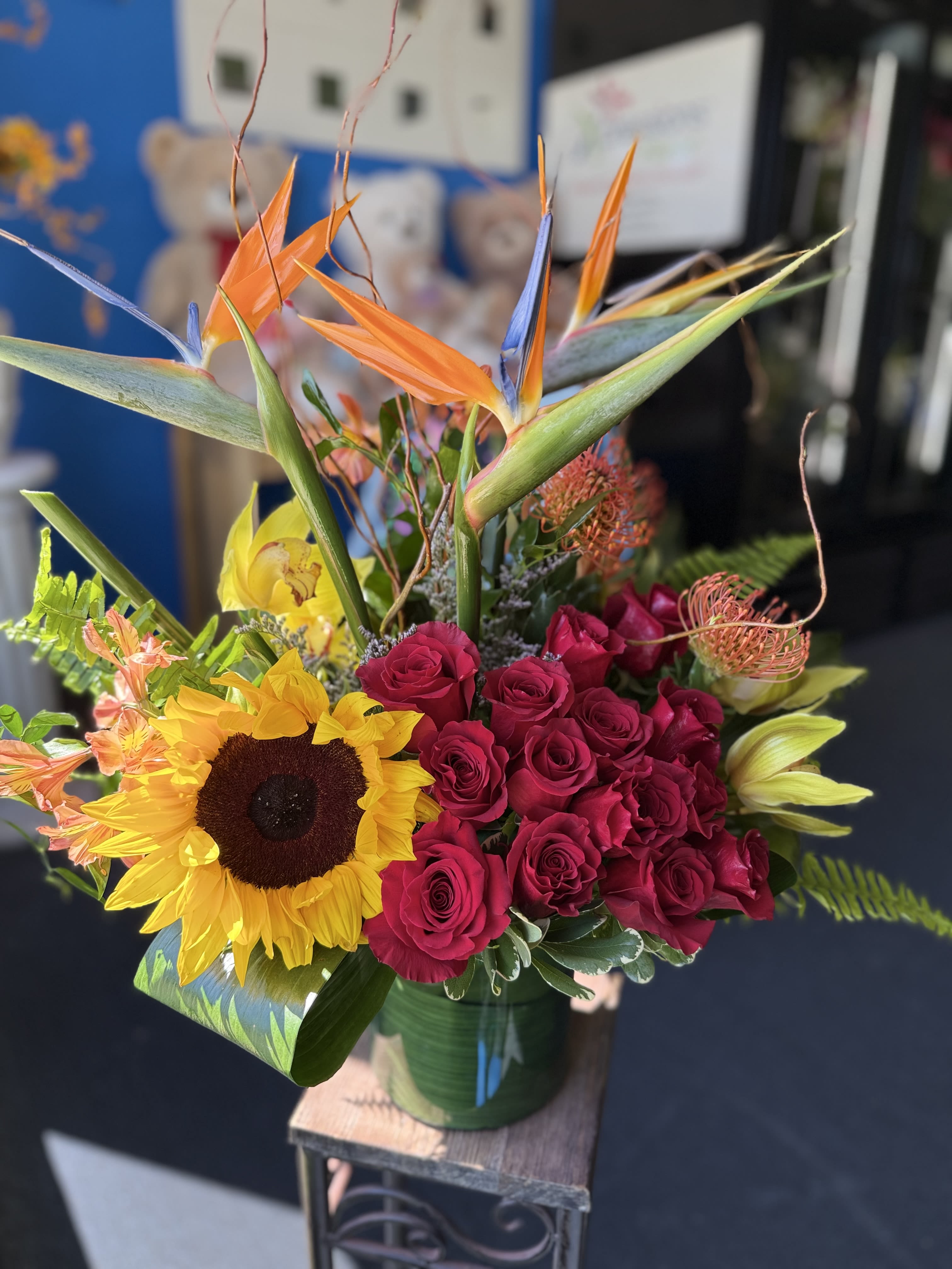 Tropical arrangement with birds of paradise, red roses, sunflower and lilies in a glass vase