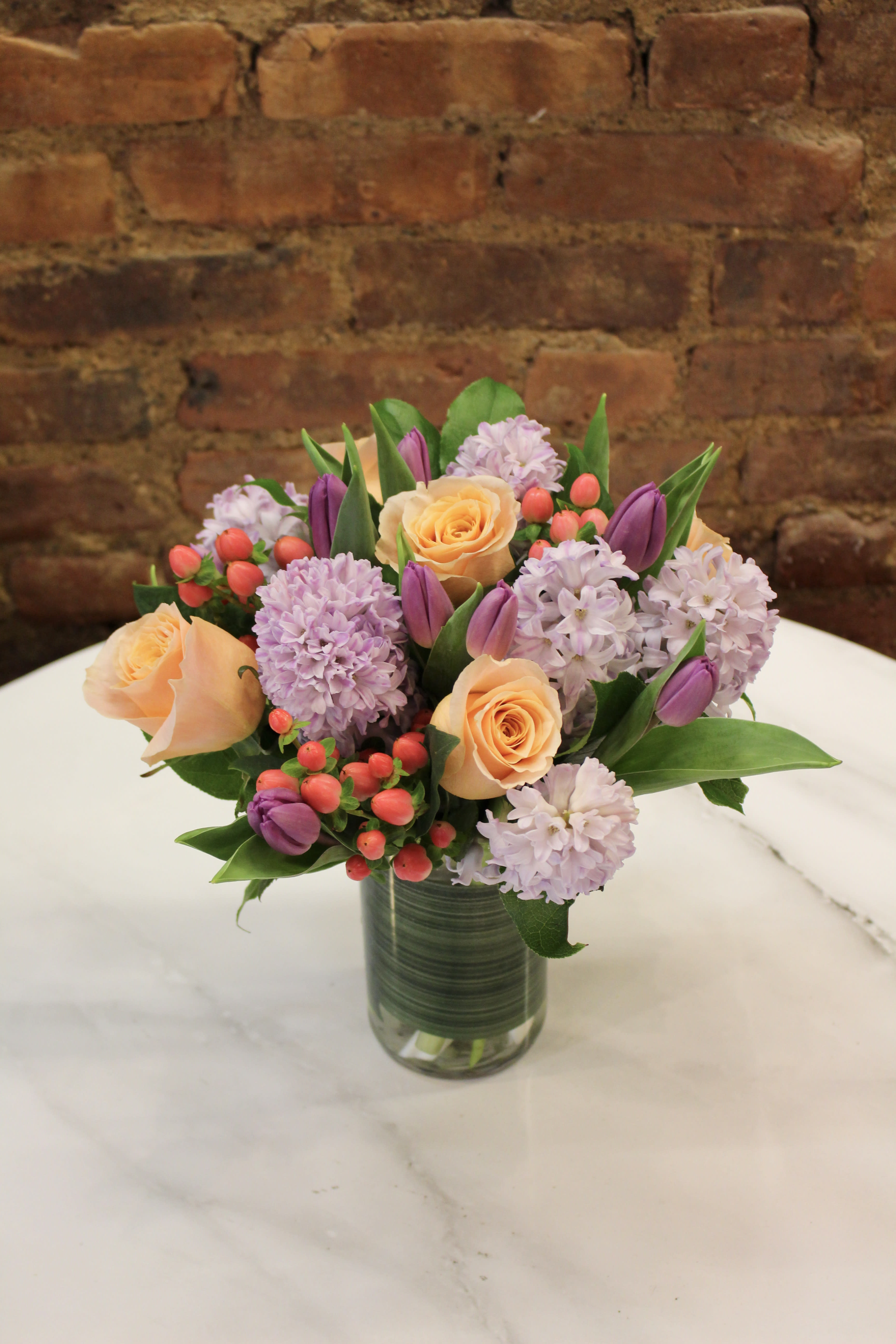 Bouquet of peach roses, lavender blooms, and purple tulips in a glass vase